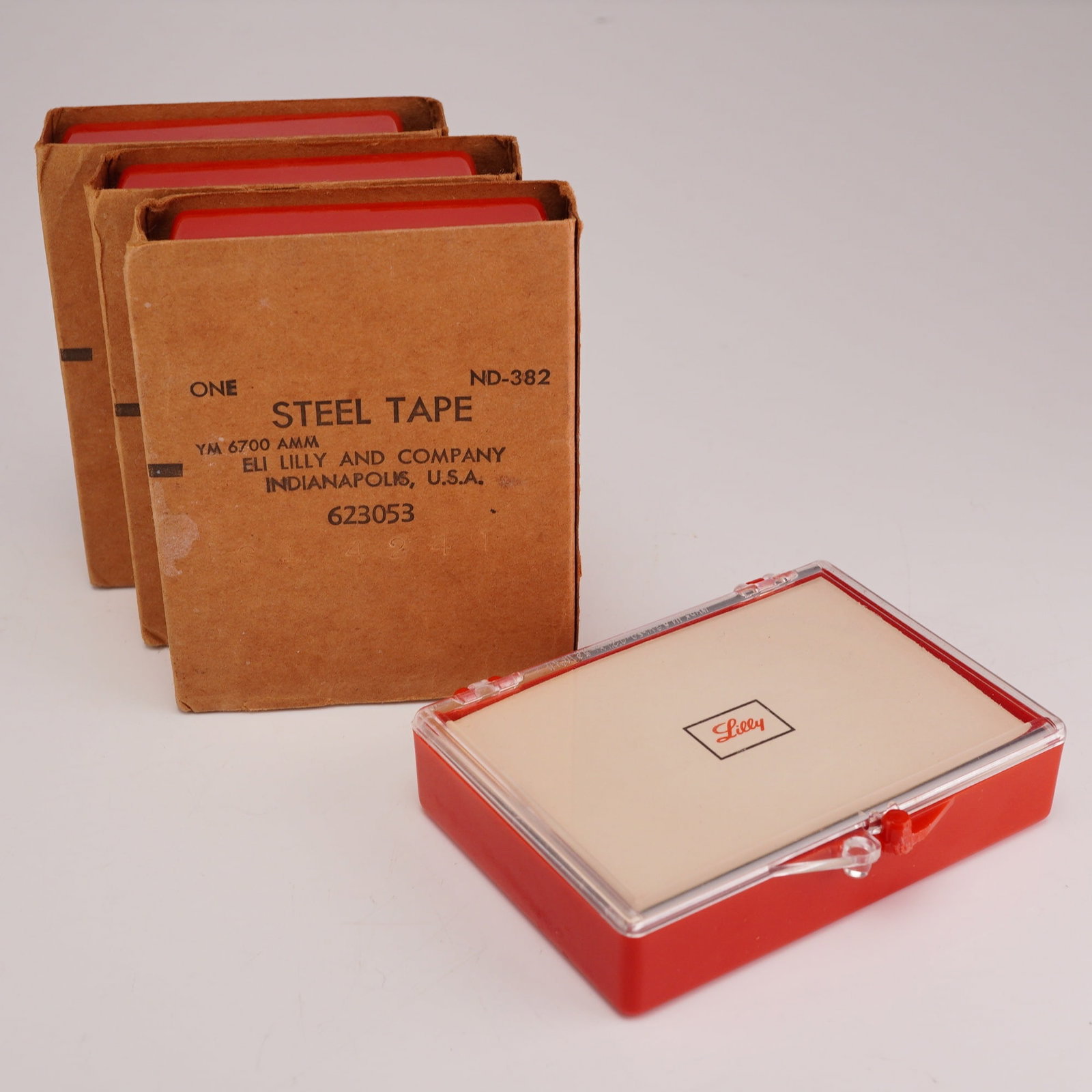4pc Eli Lilly and Company Steel Tape Measurers: A set of four promotional steel tape measures manufactured for Eli Lilly and Company of Indianapolis, Indiana. Each unit features a circular steel tape housed in a metal and plastic casing with a red,