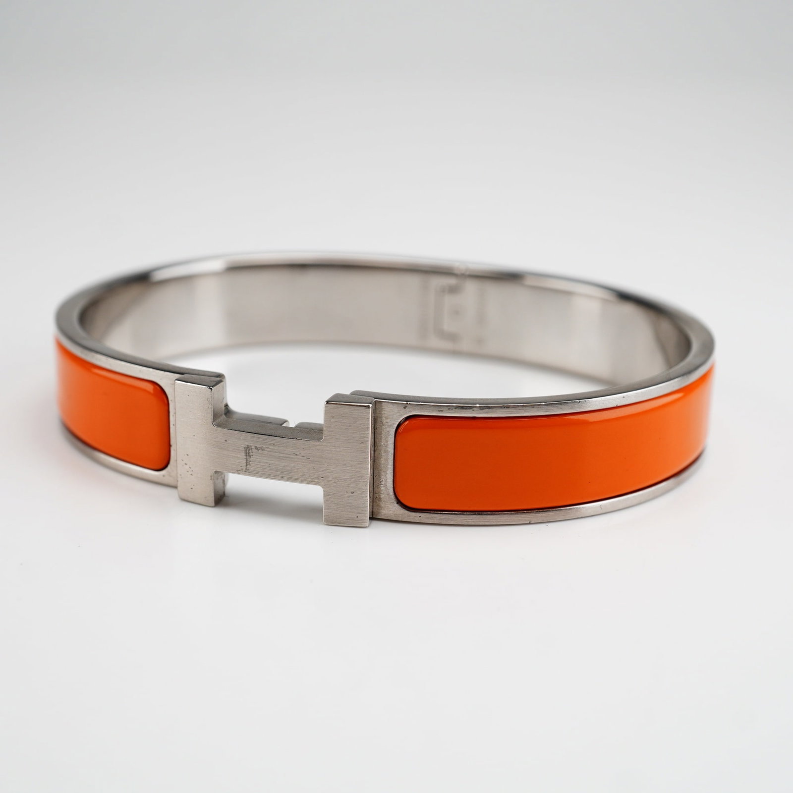 Hermes Clic H Orange Enamel Palladium-Plated Bracelet: This Hermes bangle bracelet is finished with orange enamel on palladium-plated hardware. It opens and closes with an H toggle clasp. Stamped Hermes and Made in France on the inside. Dimensions: