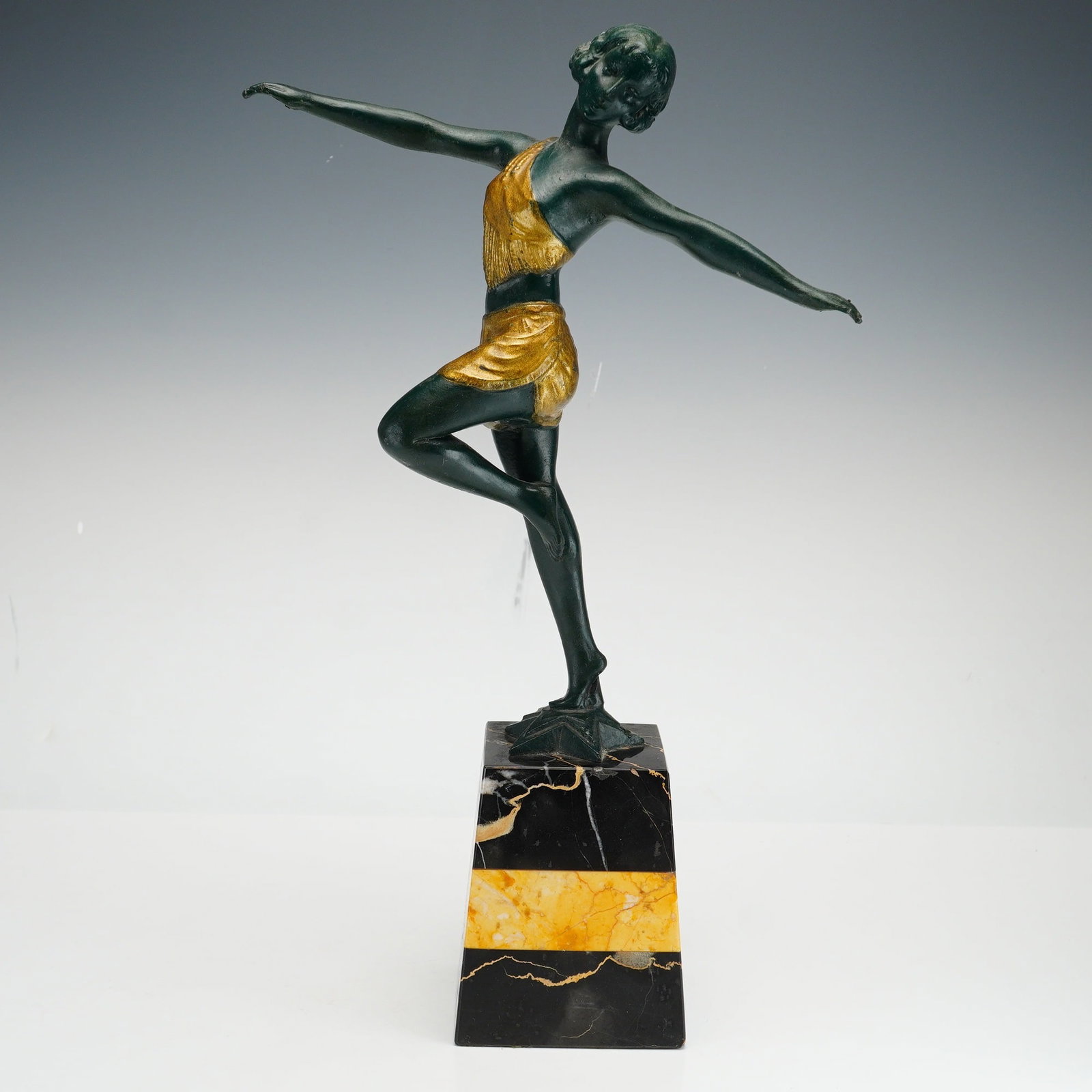 In the Style of Josef Lorenzl (Austrian 1892-1950) Art Deco Bronze & Gilt Dancer Sculpture: This Art Deco bronze sculpture in the style of Josef Lorenzl depicts a female dancer in a dynamic pose with outstretched arms and one leg raised. The figure is cast in bronze and features a dark green