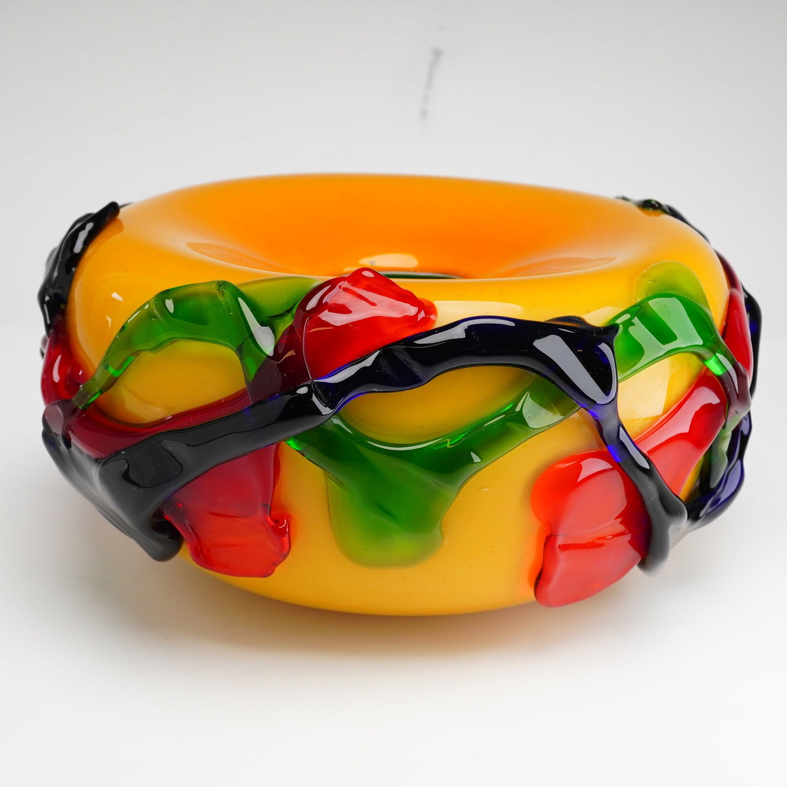 Murano Style Rainbow Original Art Glass Vase: This original art glass vase is a hand-blown vessel featuring a compressed globular form with a central circular aperture at the top. The body is constructed from opaque yellow-orange glass. The exter