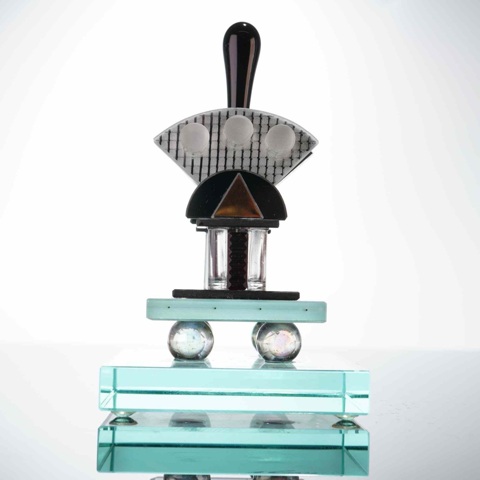 George Ponzini Postmodern Studio Art Glass Perfume Bottle: This architectural studio glass work is executed in a Postmodern style reminiscent of the Memphis Milano movement. The piece is constructed from multiple geometric glass components. The base is a thic