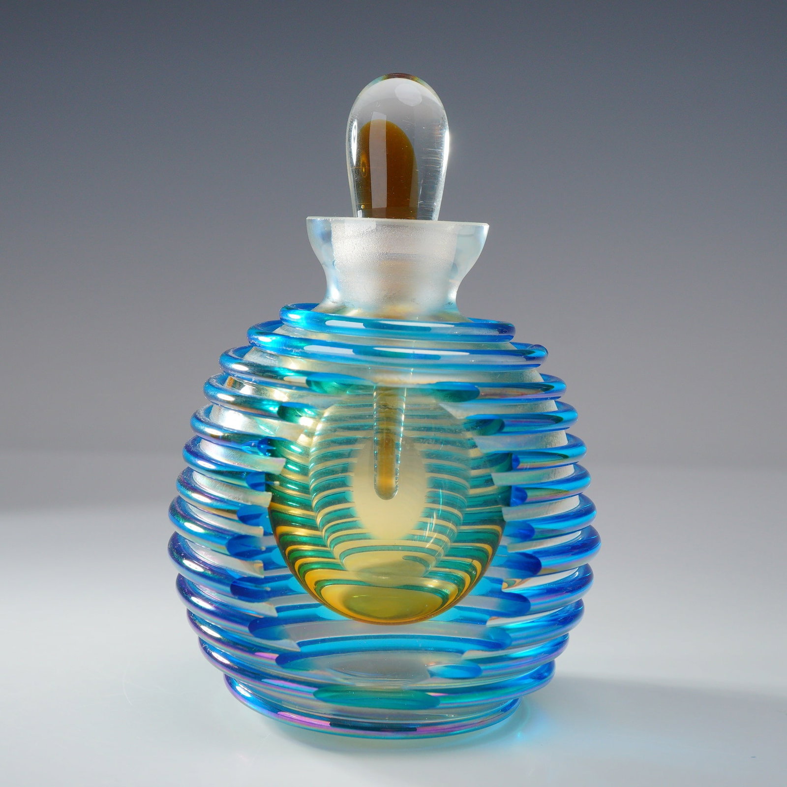 Murano-Style Art Glass Perfume Bottle: A rounded form, featuring a spiraling blue pattern over an iridescent ground. The bottle is accompanied by a clear and amber-colored glass stopper, which function as an applicator. Dimensions: 3.25"L 