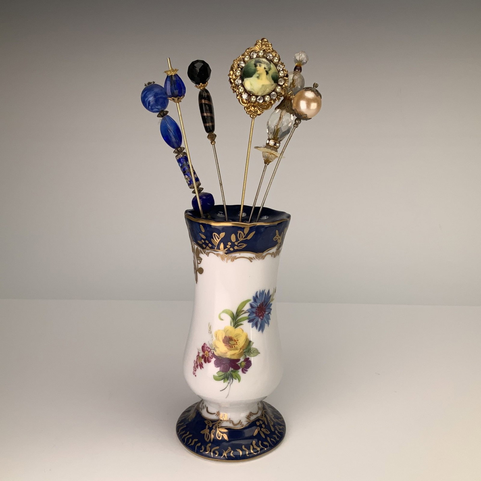 7pc Limoges France Hat Pin Holder and Hat Pins: This lot features a Limoges porcelain hatpin holder and an assortment of six vintage hatpins. The porcelain holder is designed in a pedestal style with a flared, scalloped rim and a stepped circular f