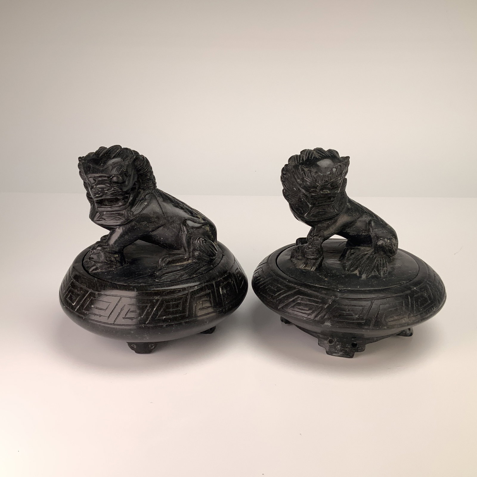 A Pair of Carved Black Stone Foo Dog Trinket Boxes: A pair of carved stone Foo Dog trinket boxes fashioned as lidded tripod vessels in a traditional Chinese style. Each piece is carved from a dark, polished stone, finished to a deep black color. The li