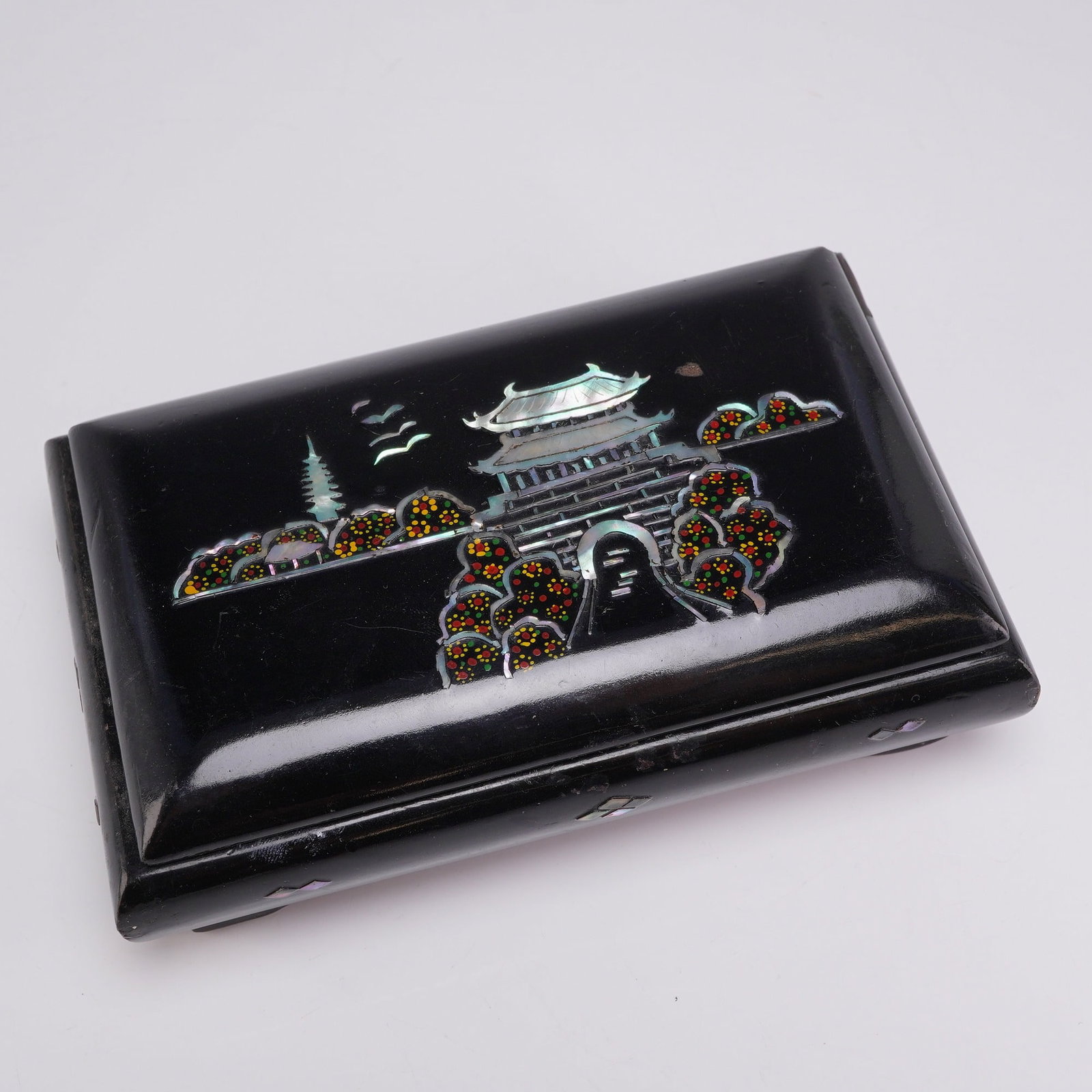 Mother-of-Pearl Inlaid Black Lacquer Lidded Box: This lidded box is constructed of wood and finished in a deep black lacquer. The exterior features elaborate mother-of-pearl inlay work. The central motif on the lid depicts a traditional architectura