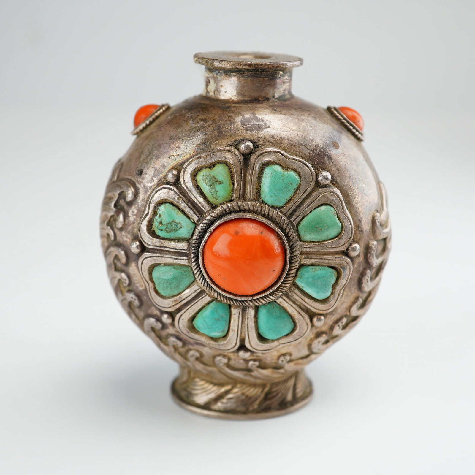 Mongolian Silver Repousse Snuff Bottle, Flower, Dragon Bird in Waves: A Mongolian silver repousse snuff bottle featuring a dragon-bird figure amid waves on one side and a floral design on the other, with turquoise stones as petals and a round coral cabochon at the cente