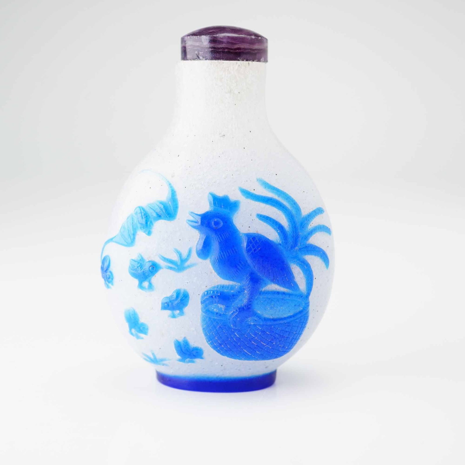 Peking Glass Snuff Bottle, Blue Overlay Deer, Bats, and Chicken: A round, clear, speckled Peking glass snuff bottle featuring a blue relief overlay portraying a chicken on a basket, chicks, lingzhi mushroom, bats, a deer, and botanical elements. It is topped with a