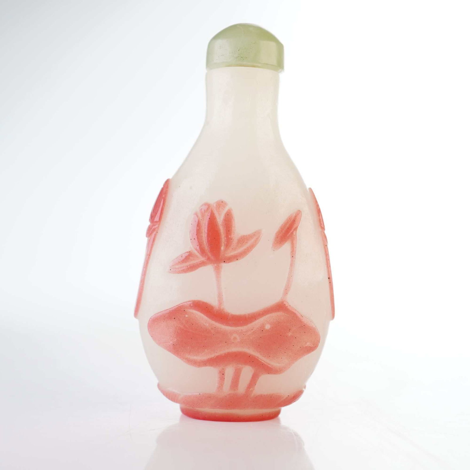 Peking Glass Snuff Bottle, Pink Overlay Lotus and Faux Lion Handles: An off-white Peking glass snuff bottle decorated with pink overlay reliefs of lotus flowers and lotus leaves with simulated handles. It is topped with a domed, sage green jade-like stopper. Dimensions