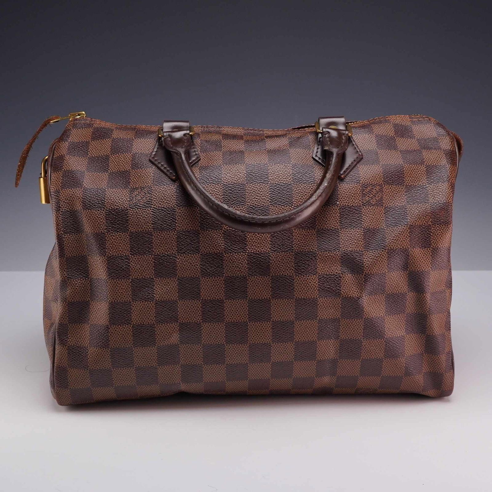 Louis Vuitton Brown Damier Ebene Speedy Bag with Padlock: This authentic Louis Vuitton Speedy handbag is crafted in the signature Damier Ebene coated canvas with dark brown leather trim. This classic "doctor bag" silhouette features dark brown rolled leather