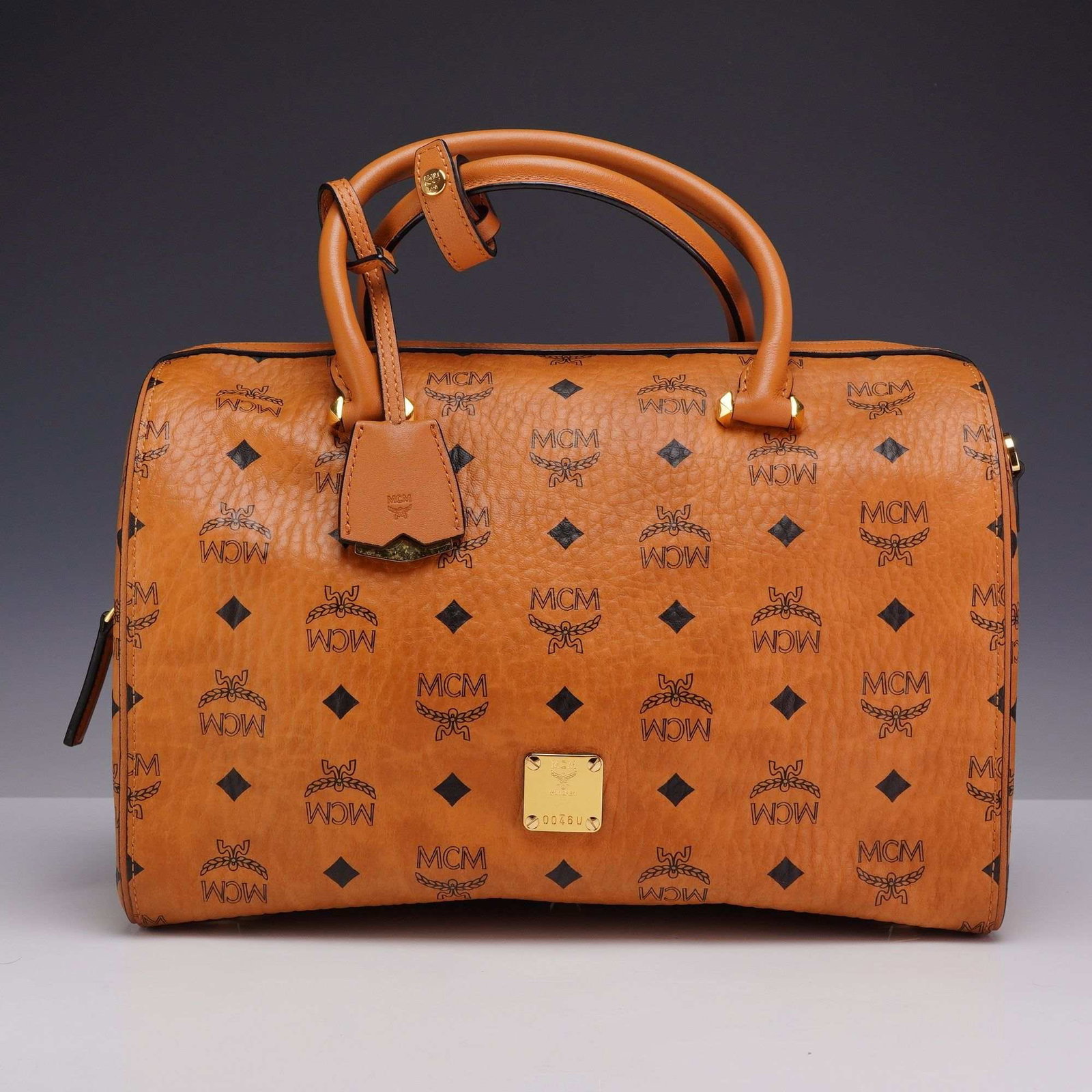 MCM Cognac Visetos Coated Canvas Boston Handbag with Shoulder Strap: This MCM Boston bag is crafted from signature cognac-colored Visetos monogrammed coated canvas with leather trim and gold-tone hardware. The exterior features double rolled leather top handles and a t