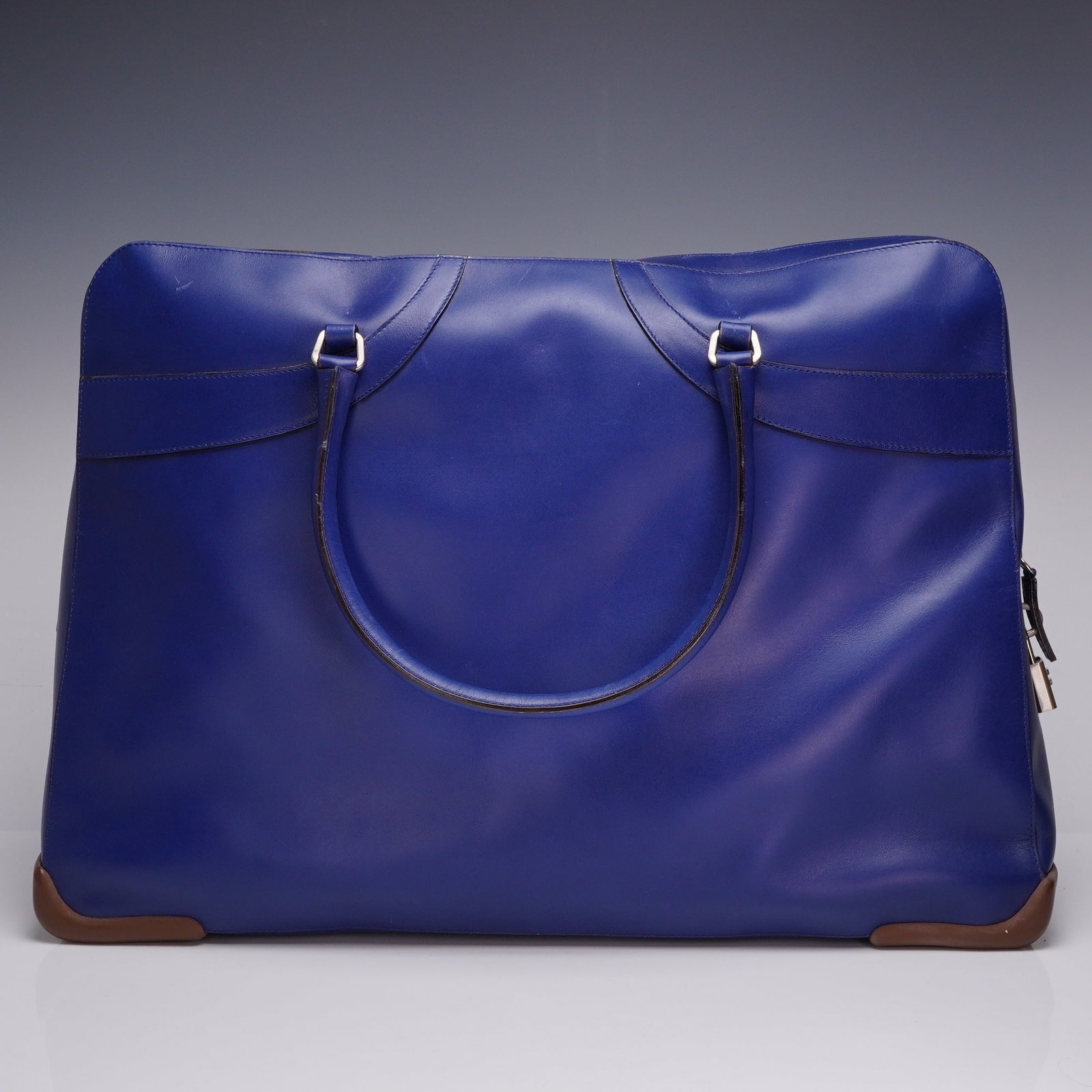Prada Cobalt Blue Leather Travel Weekender Satchel: A large-format travel bag by Prada, crafted from cobalt blue smooth calfskin leather with contrasting brown leather accents. The design features double rolled leather top handles and a silver-tone top