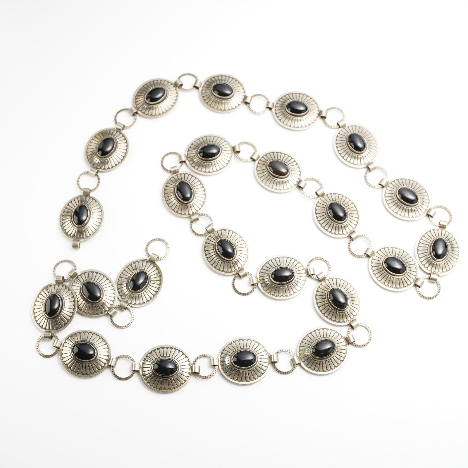 Southwest Style Silver Tone Metal Concho Chain Belt with Black Cabochons: A Southwest-style concho chain belt crafted from silver-tone metal. The belt features seventeen oval conchos, each centered with a bezel-set oval black cabochon, possibly onyx. The metal surrounding e