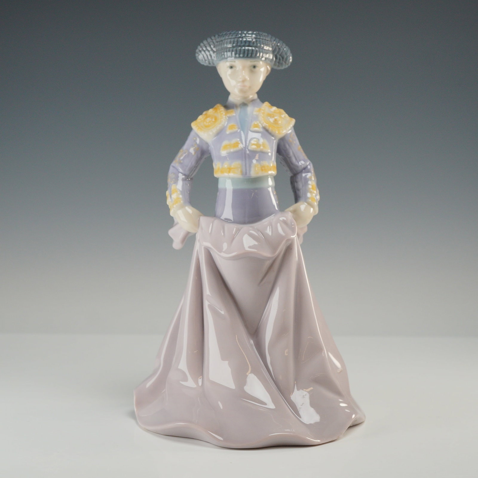 Lladro Porcelain Figurine Young Torero 01006438 with Original Box: Designed by sculptor Francisco Catala, the piece depicts a young bullfighter in a traditional traje de luces (suit of lights) holding a pink and yellow cape. The figure is handcrafted in Spain from po