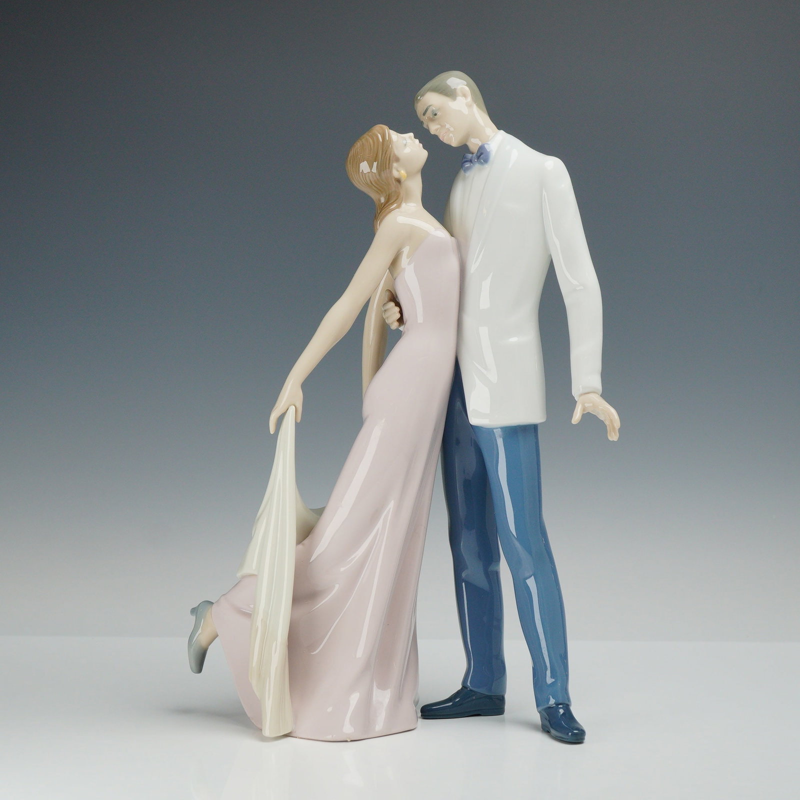 Lladro Porcelain Figurine, Happy Anniversary 01006475: This Lladro glazed porcelain figurine, identified as the Happy Anniversary model 6475, depicts a couple in formal attire engaged in a dance. The male figure is dressed in a white dinner jacket with a 