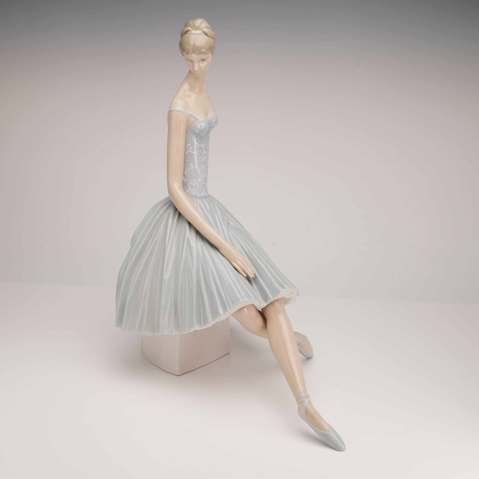 Lladro Waiting Backstage Porcelain Sculpture, 4559: This glazed porcelain figurine, titled Waiting Backstage (model 1004559), is a production of the Spanish manufacturer Lladro, designed by artist Fulgencio Garcia. The piece depicts a seated ballerina 