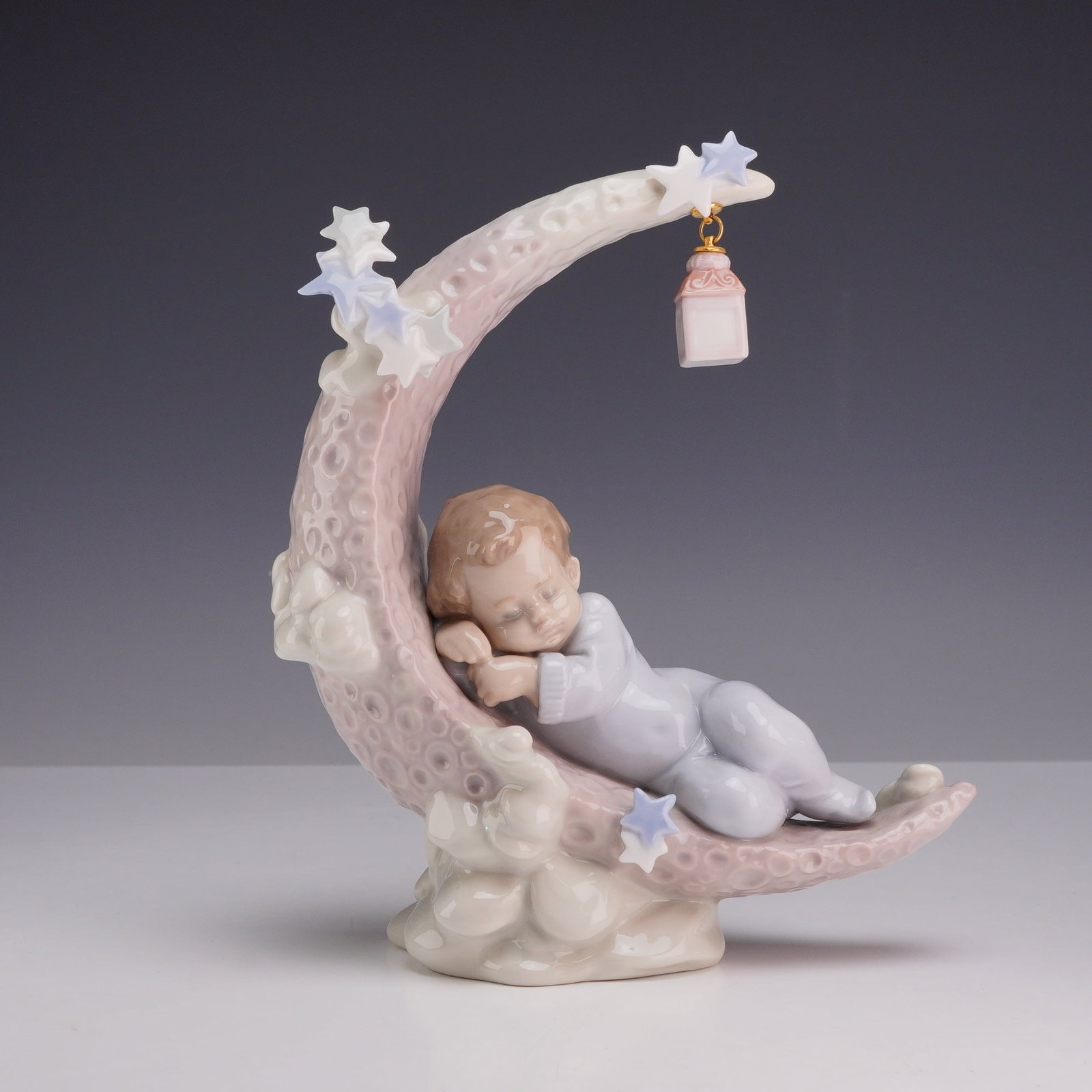 Lladro Heavenly Slumber Porcelain Figurine, Model 6479: Lladro glazed porcelain figurine titled Heavenly Slumber, model number 6479. The piece depicts a young boy in pale blue pajamas sleeping on a textured, pink-toned crescent moon. The moon is decorated 