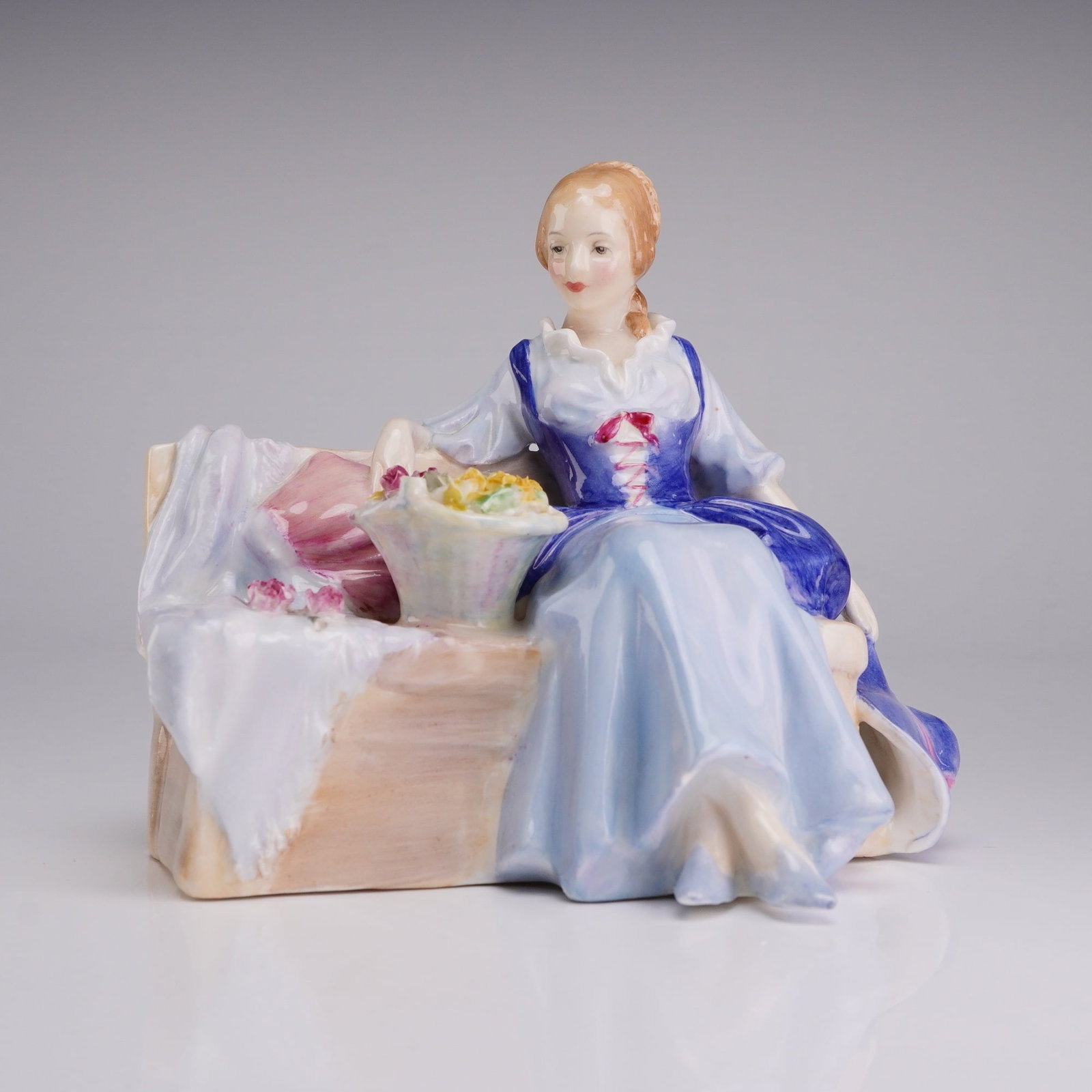 Royal Doulton Figurine, Midsummer Noon HN1900: A Royal Doulton bone china figurine titled Midsummer Noon, model HN1900. This polychrome glazed porcelain piece depicts a young woman in 18th-century style dress seated on a garden bench. She wears a 