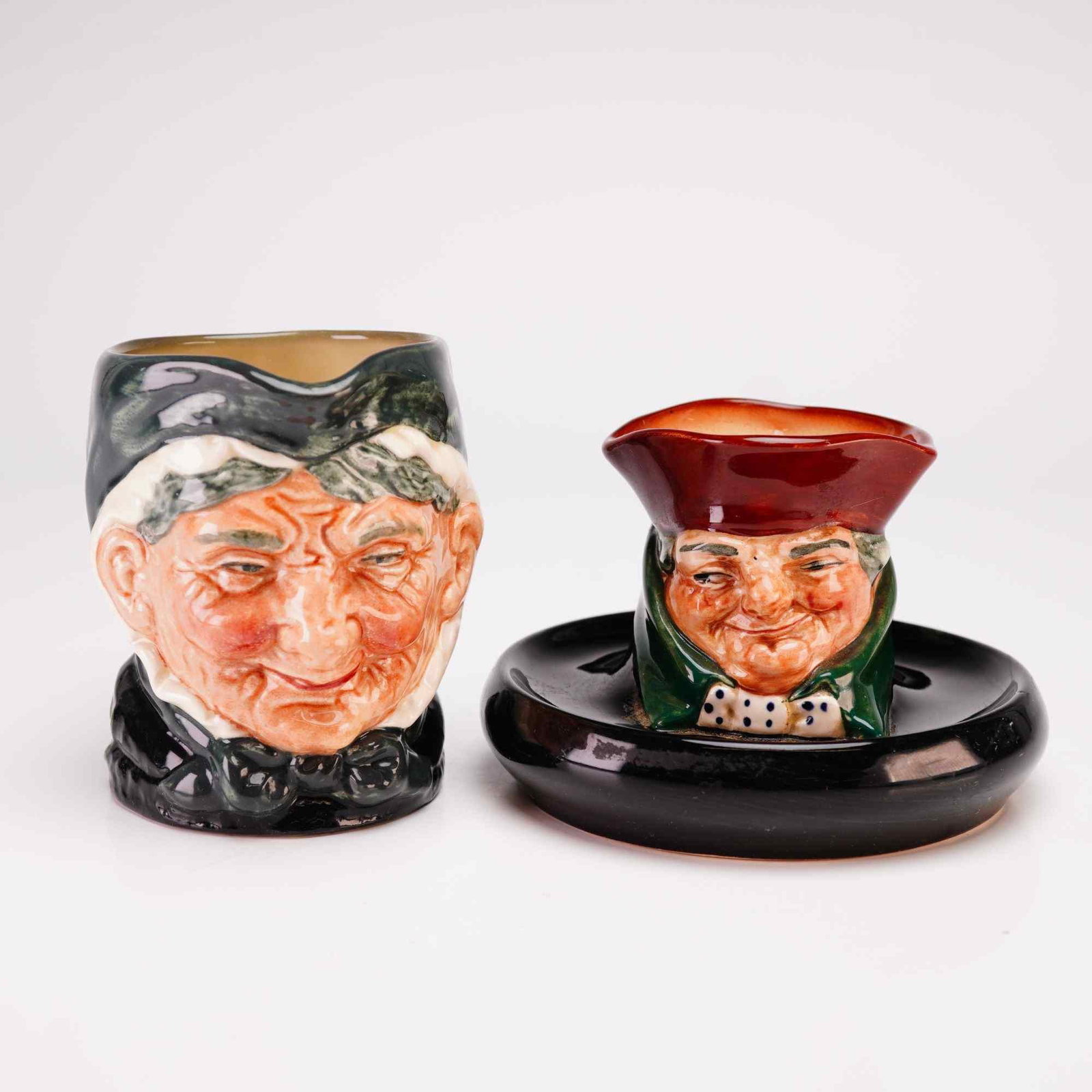 Royal Doulton Granny and Old Charley Character Ware Grouping: This 2pc Royal Doulton grouping includes an Old Charley ashtray and a Granny small jug. Produced by Royal Doulton in Burslem, England, these glazed earthenware items feature molded character forms dec
