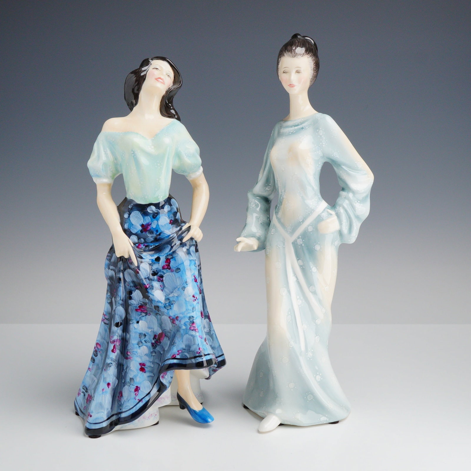2pc Royal Doulton Porcelain Figurines, Carmen HN 2545 and Boudoir HN 2542: This pair of glazed porcelain figurines is produced by Royal Doulton, England. The first figurine, Carmen (HN 2545), depicts a woman in a dramatic pose with her head tilted back, lifting the hem of he