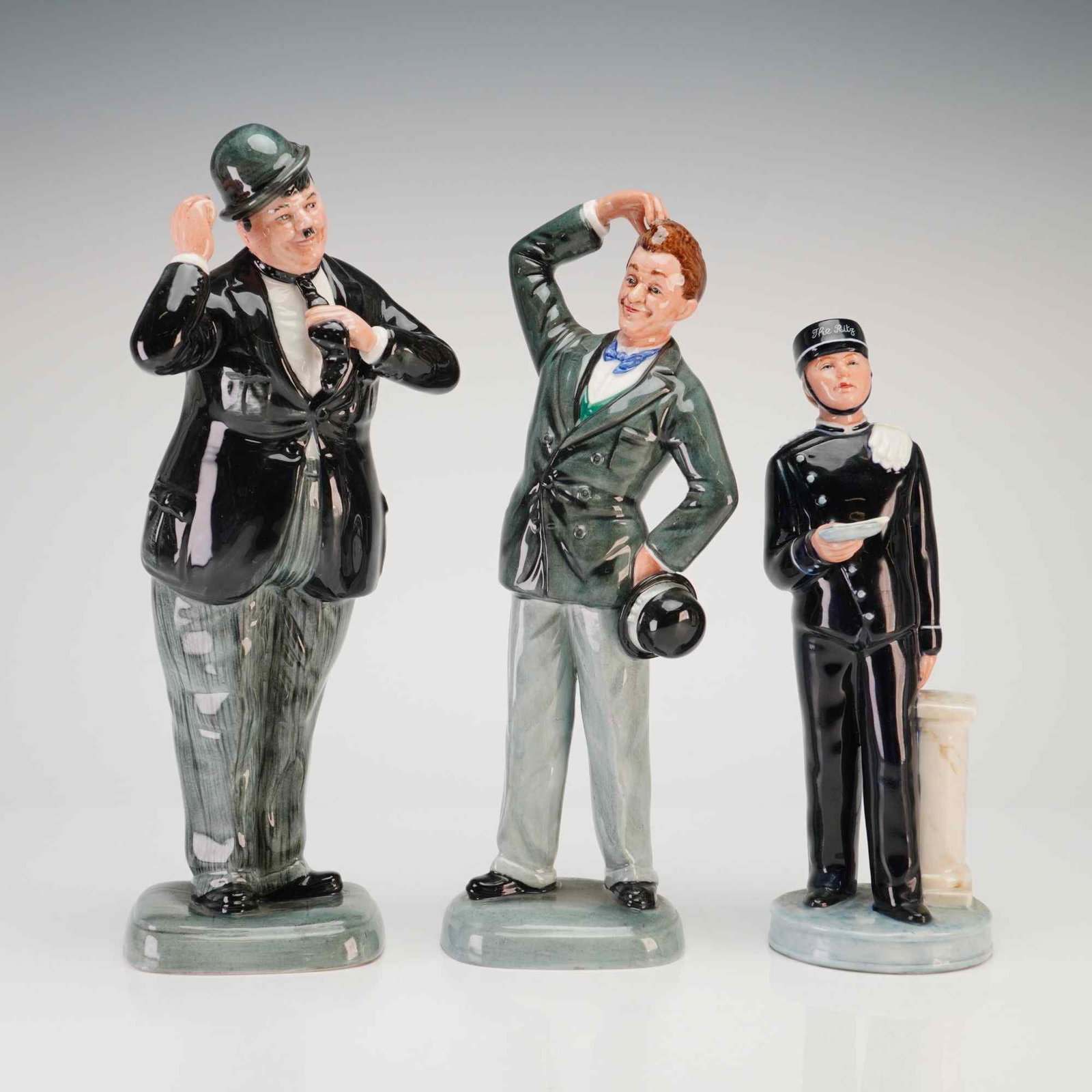 Three Royal Doulton Figurines Oliver Hardy HN 2775 Stan Laurel HN 2774 and Ritz Bell Boy HN 2772: This lot features three Royal Doulton hand-painted glazed porcelain figurines modeled by William K. Harper. The collection includes the iconic comedy duo Stan Laurel and Oliver Hardy, accompanied by a