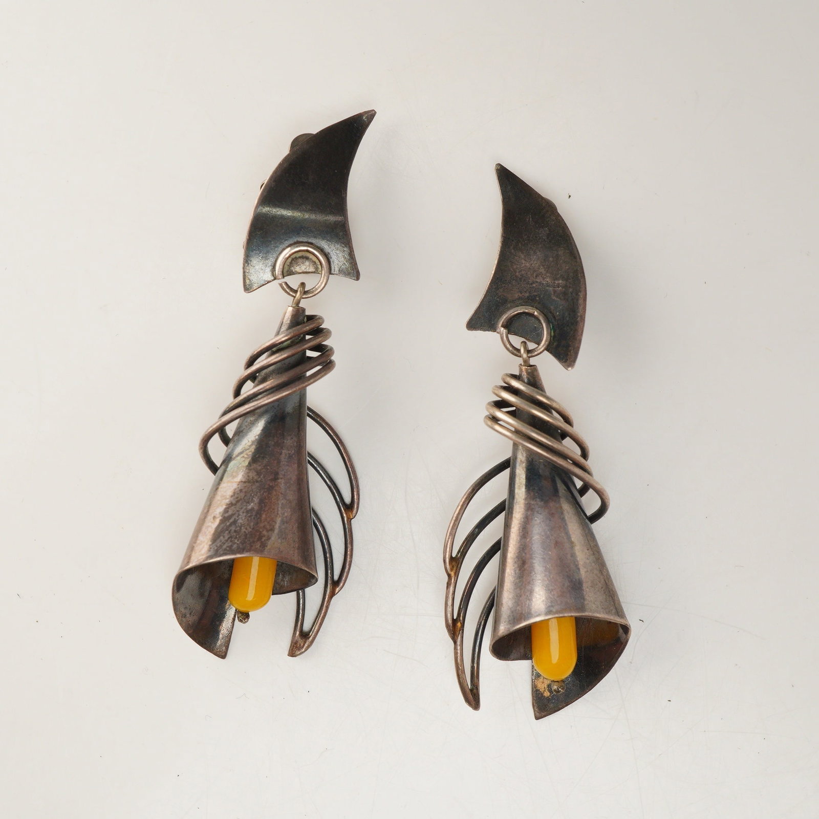 Pair of Modernist Silver-Toned Calla Lily Clip-On Drop Earrings: This matched pair of clip-on drop earrings features a modernist artisanal design with a stylized calla lily motif. Each earring is composed of a curved upper segment from which a large floral drop is 