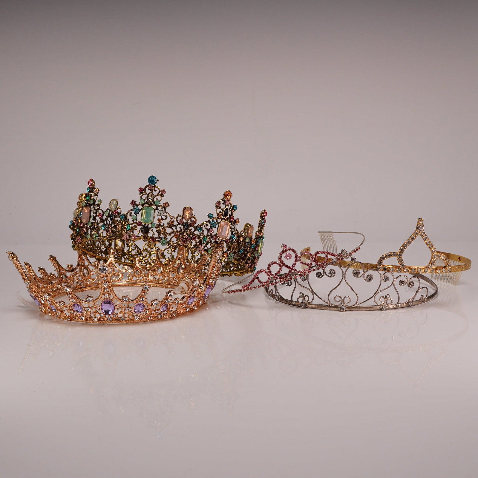 5pc Jewel Studded Ornate Tiaras and Crowns: This collection consists of five pieces of headwear, including two full-circumference crowns and three front-facing tiaras. The first piece is a full circular crown in a rose gold-tone base metal feat