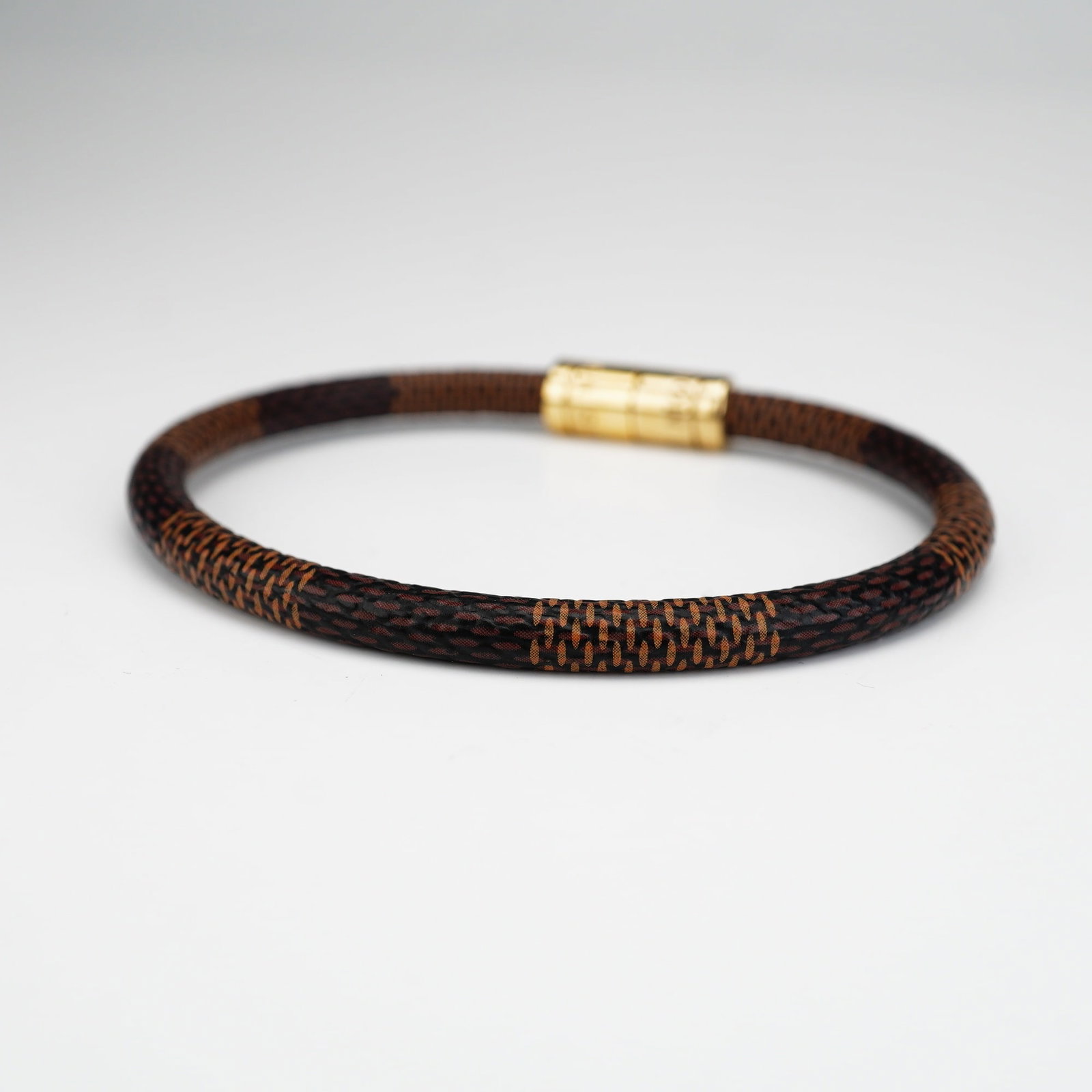 Louis Vuitton Brown Damier Ebene Keep It Bracelet: This bracelet is coated with the iconic Damier Ebene canvas, featuring the brown and tan checkerboard design. Louis Vuitton is engraved on the gold-tone metal closure. Dimensions: 2.75"L x 0.25"W Weig