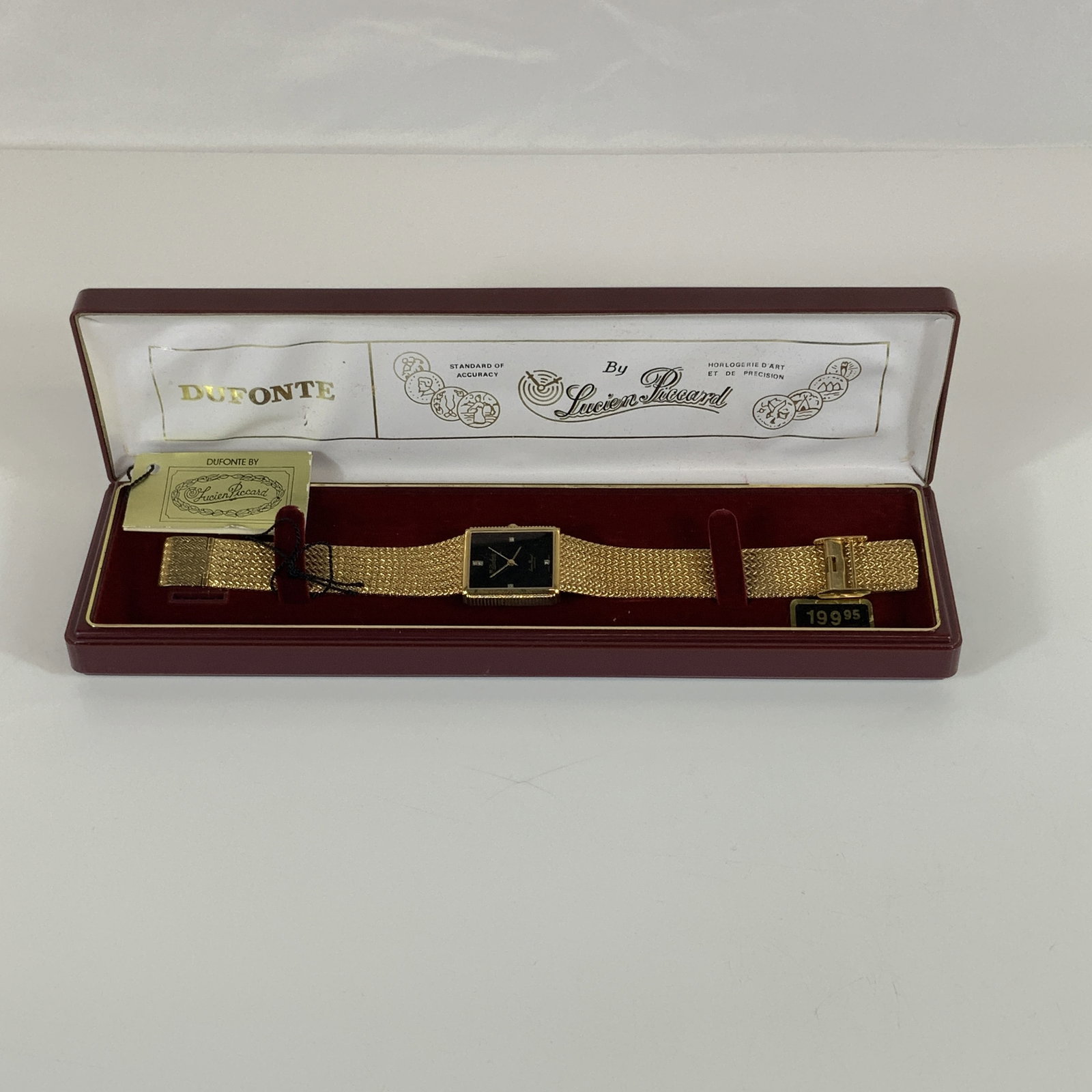 Dufonte by Lucien Piccard Gold Toned Quartz Dress Watch with Box and Tags: This is a Dufonte by Lucien Piccard rectangular dress watch. The timepiece features a gold-toned base metal bezel with a stainless-steel case back. The black dial is set with four clear stone hour mar