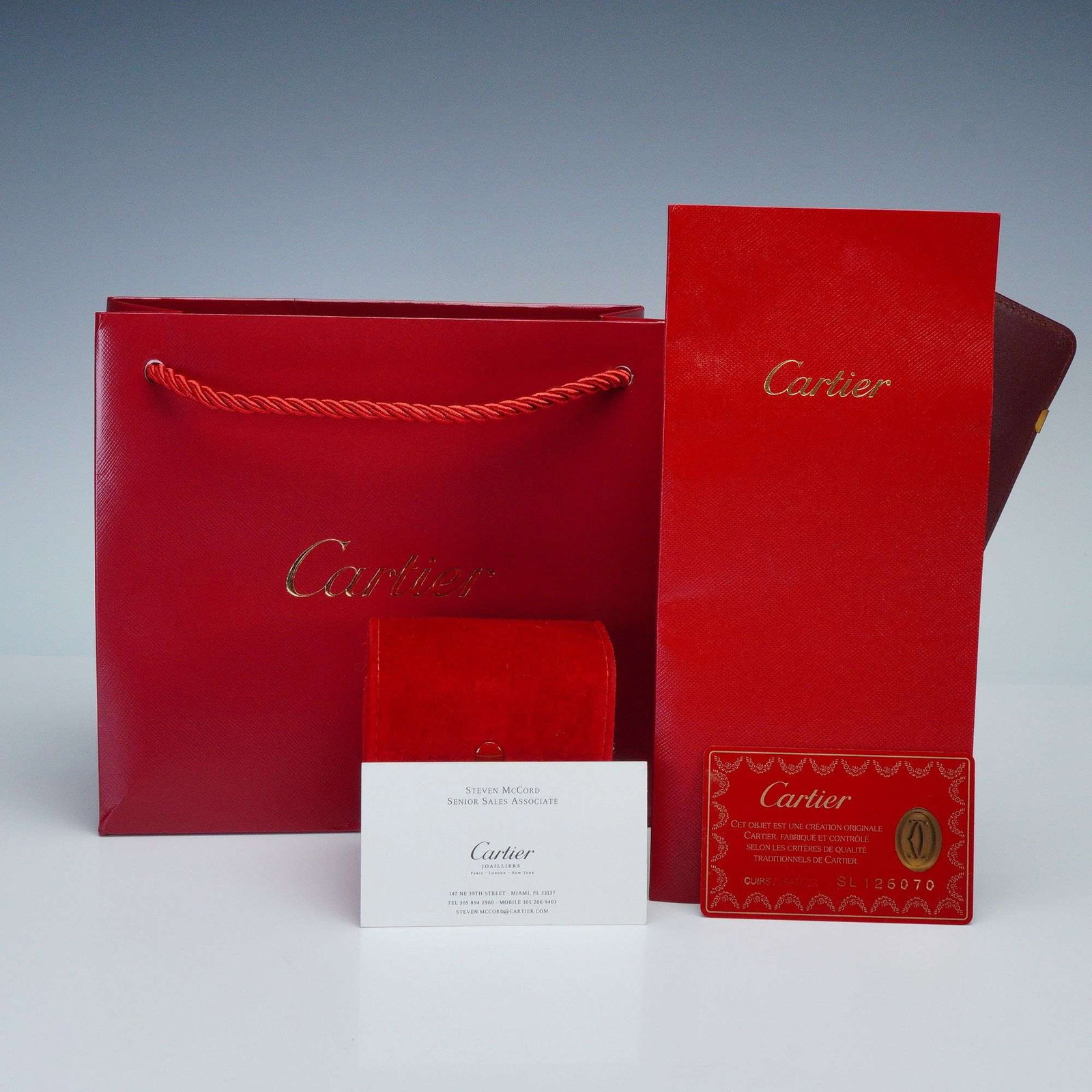 A Group of Cartier Red Branded Presentation and Authentication Materials: A group of Cartier branded presentation and authentication materials. This collection includes a red paper shopping bag with rope handles and the Cartier logo in gold, alongside a matching red texture