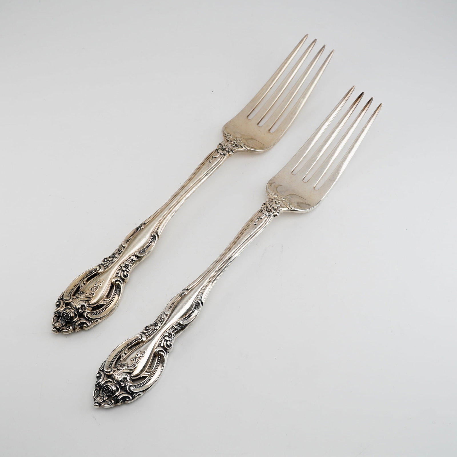 2pc Gorham Sterling Silver Dinner Forks, La Scala: An ornate Rococo Revival style, featuring heavy scrollwork and deeply chased rose floral motifs. A distinguishing feature of this design is the pierced or openwork terminal on the handle. Each fork is