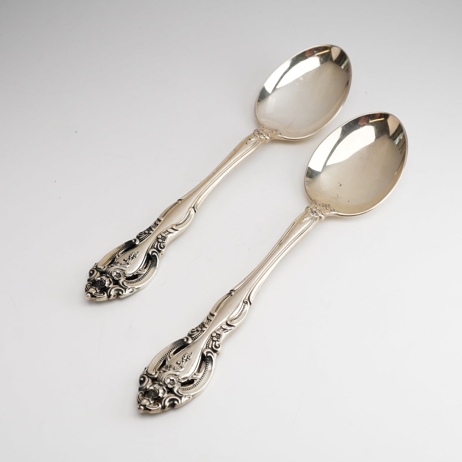2pc Gorham Sterling Silver Oval Soup Spoons, La Scala: The handles feature elaborate chasing with decorative scrolls, shell motifs, and floral clusters. The bowls are oval-shaped with a polished finish. The reverse of each handle is stamped with the Gorha