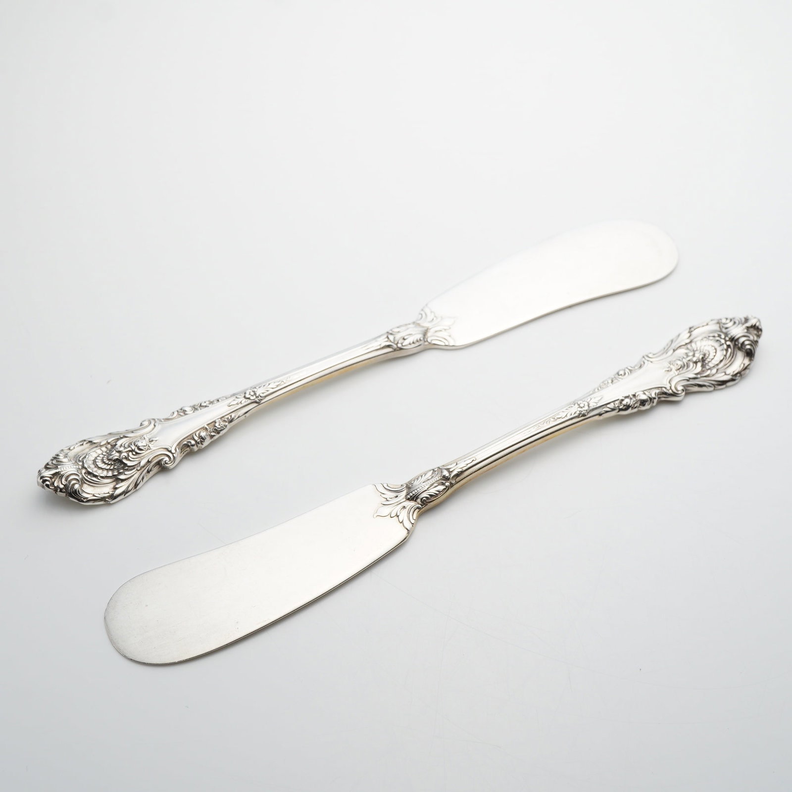 A Pair of Wallace Sterling Silver Sir Christopher Pattern Flat Handle Butter Spreaders: This pair of flat handle butter spreaders is crafted in the Sir Christopher pattern by Wallace Silversmiths. Each piece features a wide paddle blade and highly ornate handles decorated with deep-relie