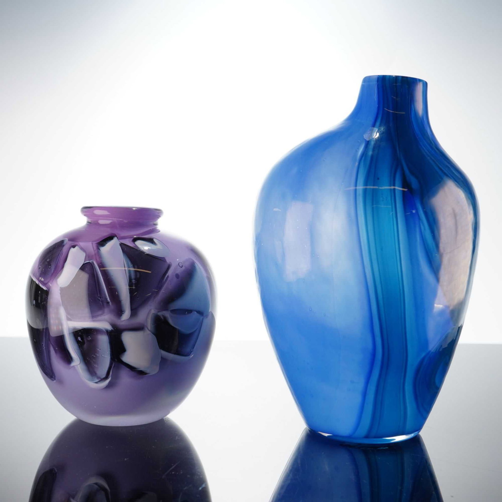 2pc Michael T. Stanton and Anthropologie Blue Swirl Art Glass Vases: The first is a small, globular hand-blown art glass vase by Michael T. Stanton. The body features a lavender base color with an abstract, mottled pattern of dark purple, black, and white inclusions. I