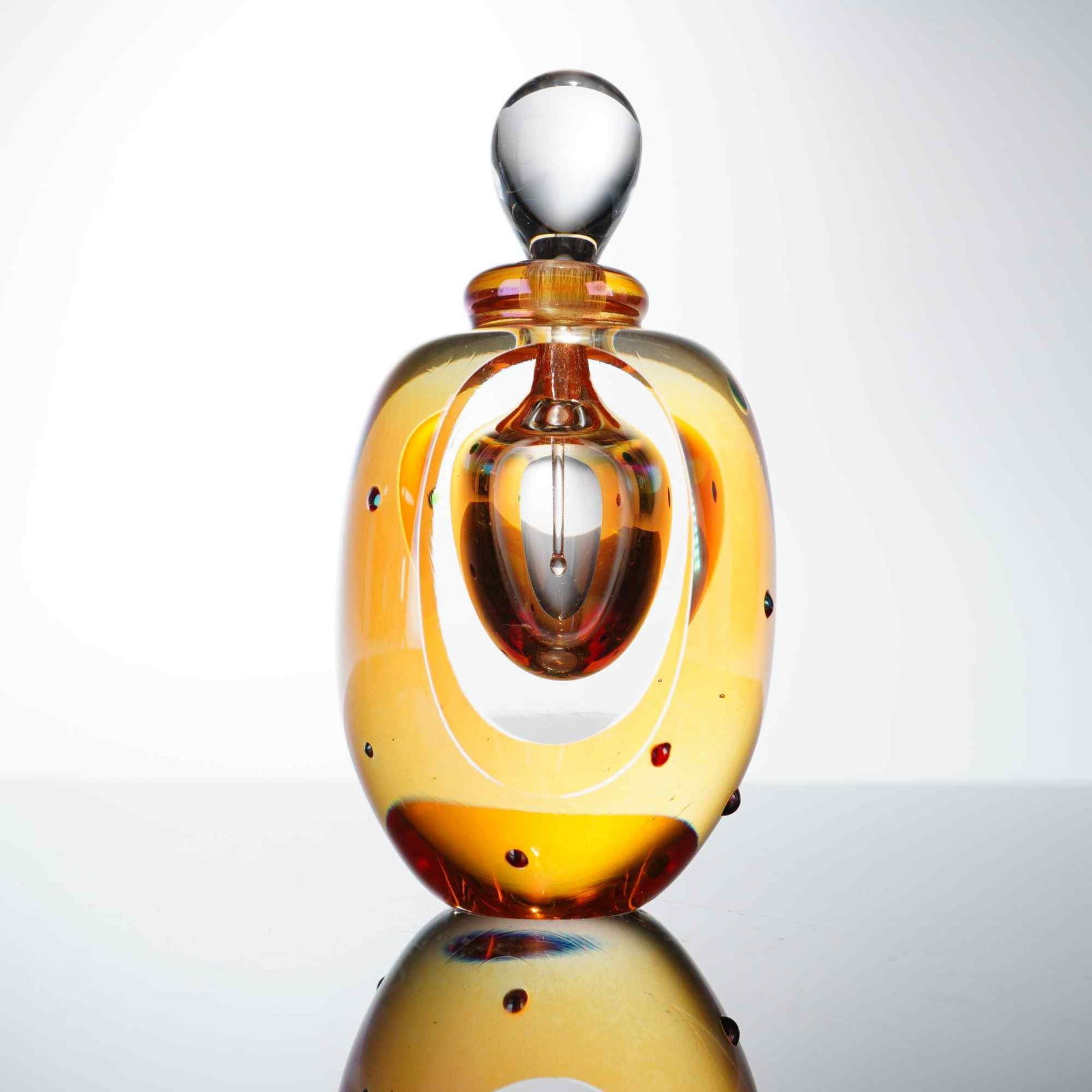 Roger Gandelman Studio Art Glass Perfume Bottle with Stopper: The piece features a thick-walled, ovoid body of amber and golden-yellow glass, with a deep red-orange color concentrated at the weighted base. The exterior is decorated with several small, applied gl