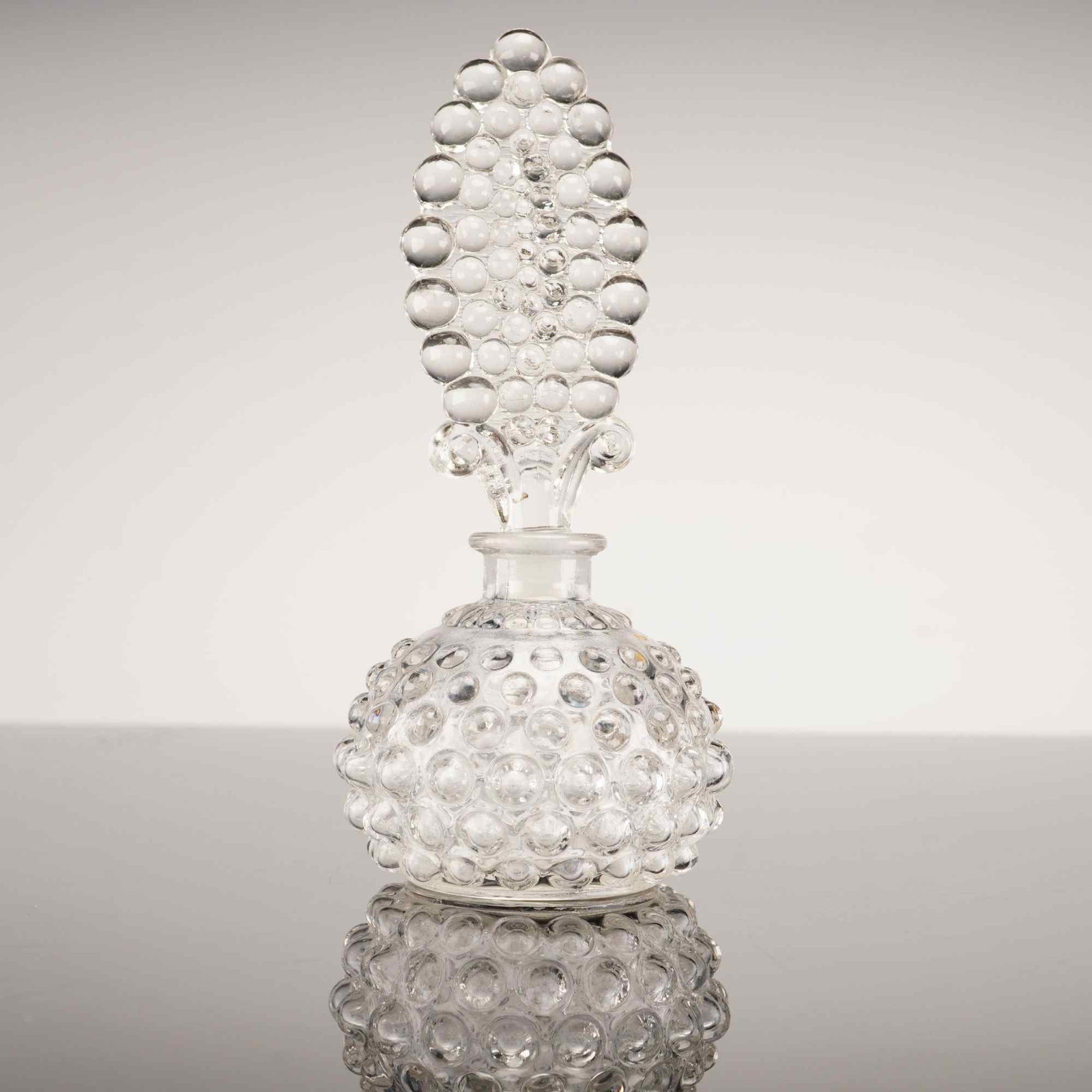 Vintage Clear Hobnail Glass Perfume Bottle with Large Fan Stopper: This vintage perfume bottle is crafted from clear glass and features a distinctive all-over hobnail pattern. The bottle is designed with a squat, globular body entirely covered in raised, rounded prot