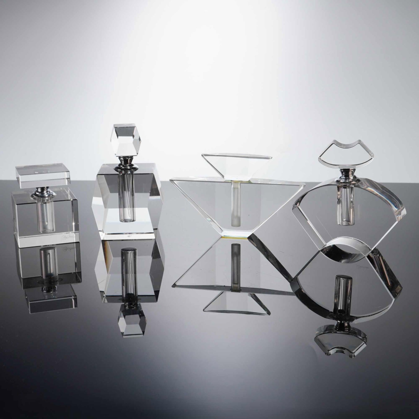 4pc Oleg Cassini and Rothfuss Clear Geometric Crystal Perfume Bottles: Each bottle is crafted from heavy, polished clear crystal with sharp-edged geometric forms and includes a metal collar at the neck to receive the stopper. The collection features a square cube bottle 