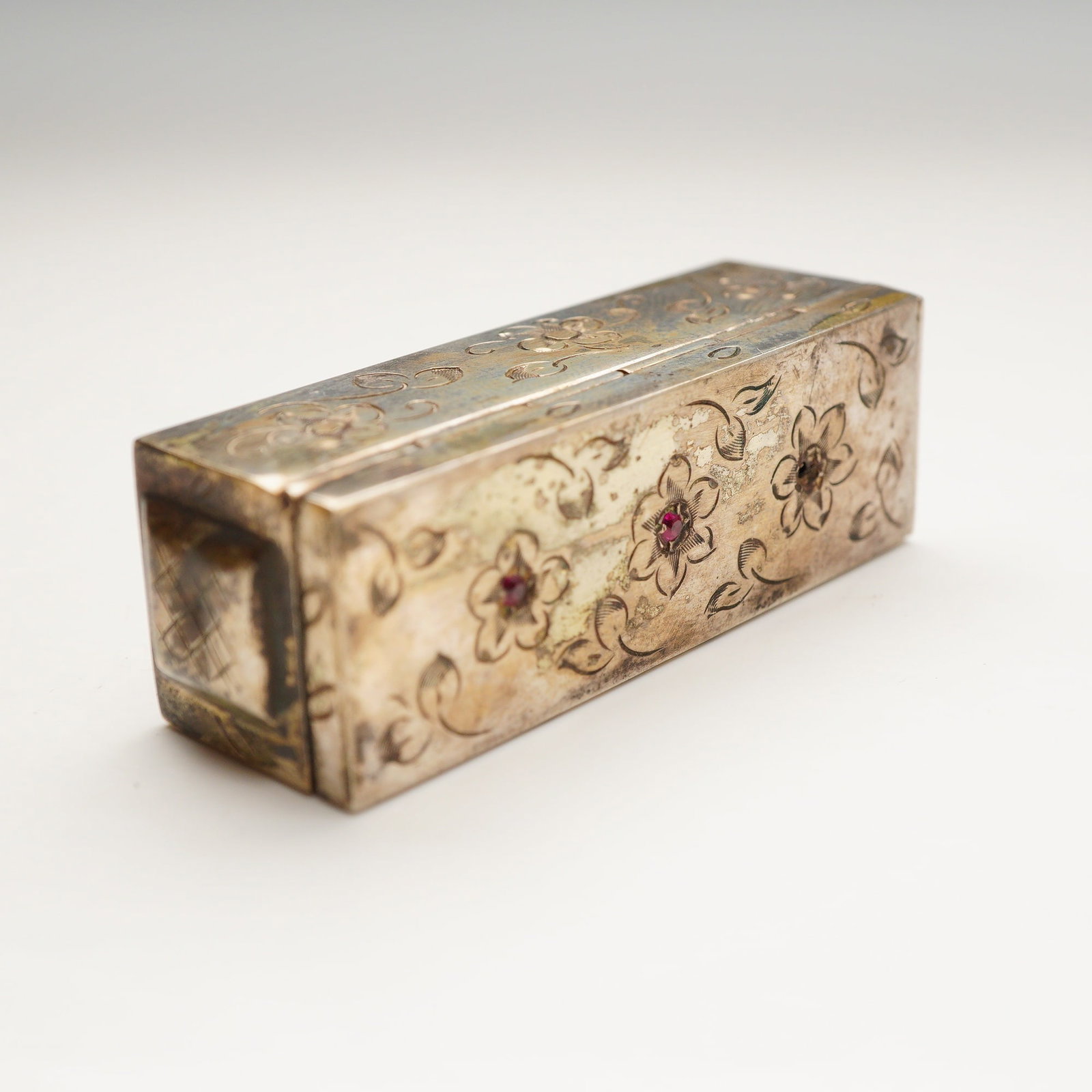 Italian 800 Silver Etched Floral Lipstick Case with Red Stones: This vintage Italian vanity accessory is a rectangular lipstick case constructed from solid .800 fineness silver. The exterior is decorated with hand-engraved floral and foliate scrollwork. The front 