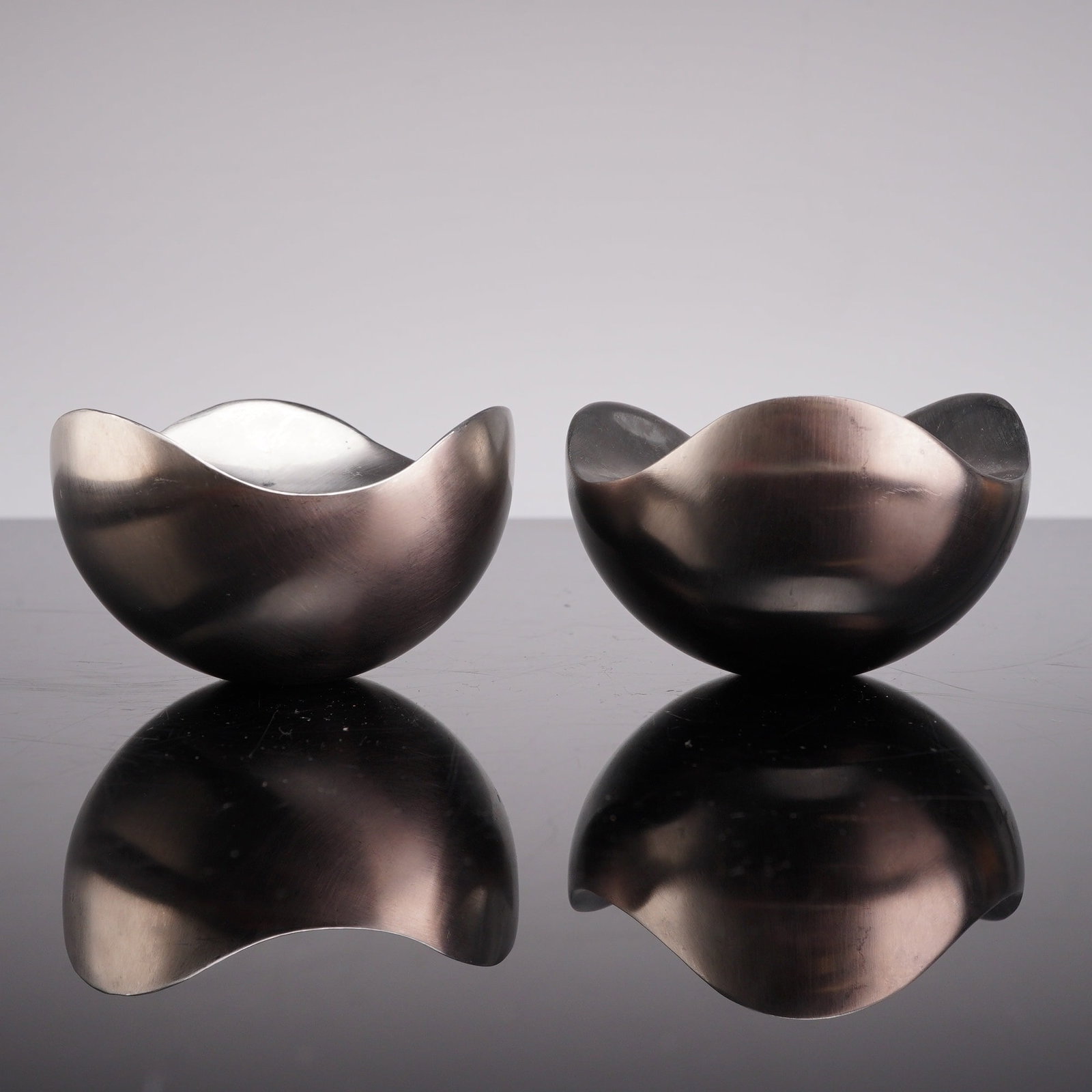 Pair of Georg Jensen Denmark Stainless Steel Bloom Candle Holders: A pair of Georg Jensen, Denmark metal candle holders from the Bloom collection. These contemporary stainless steel objects feature a minimalist ovoid design with flattened sides and a brushed satin fi