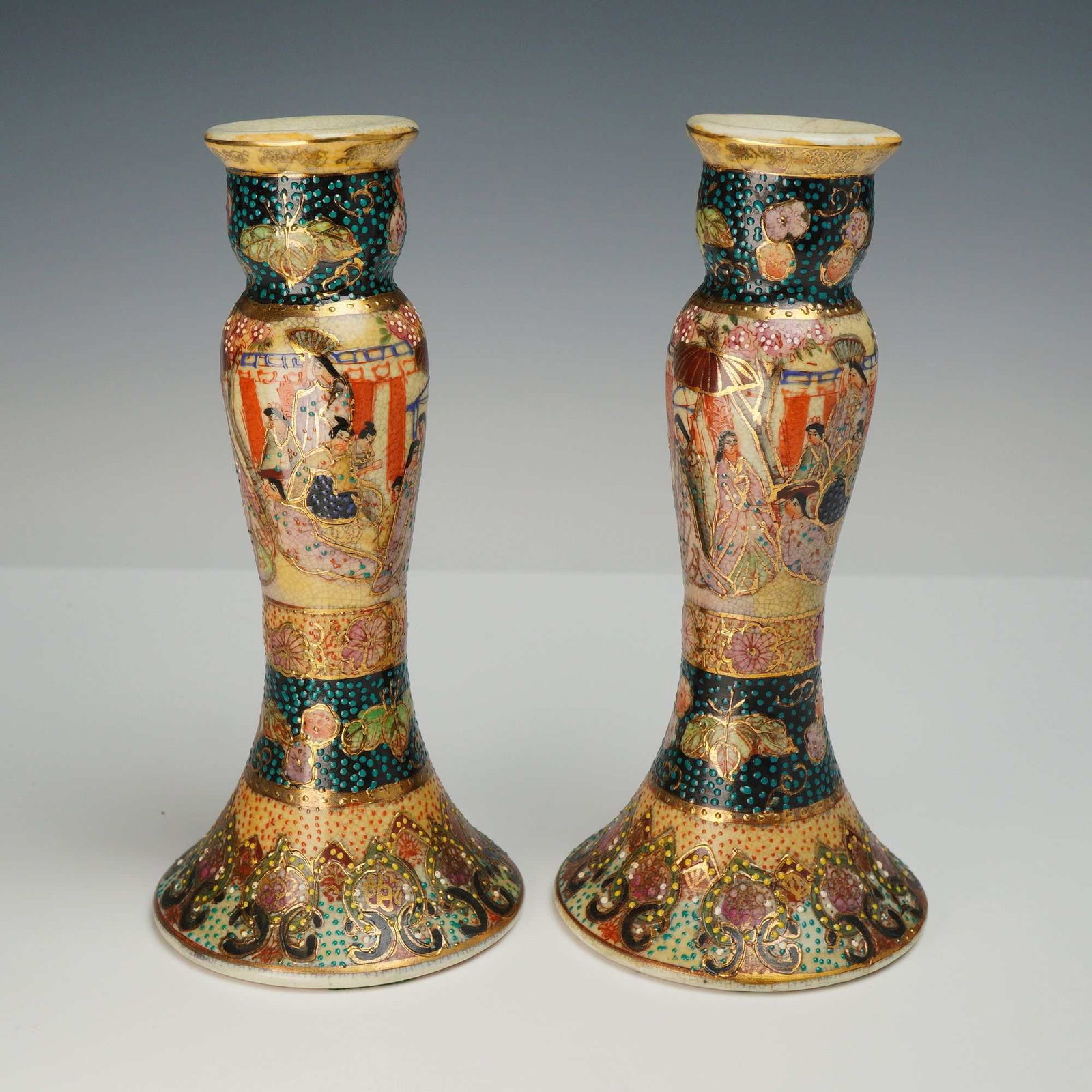 A Pair of Chinese Satsuma Earthenware Candlesticks: This pair of Satsuma candlesticks is constructed of earthenware featuring a cream-colored crackle glaze. Each candlestick is designed in a baluster form with a flared base. The central section of each