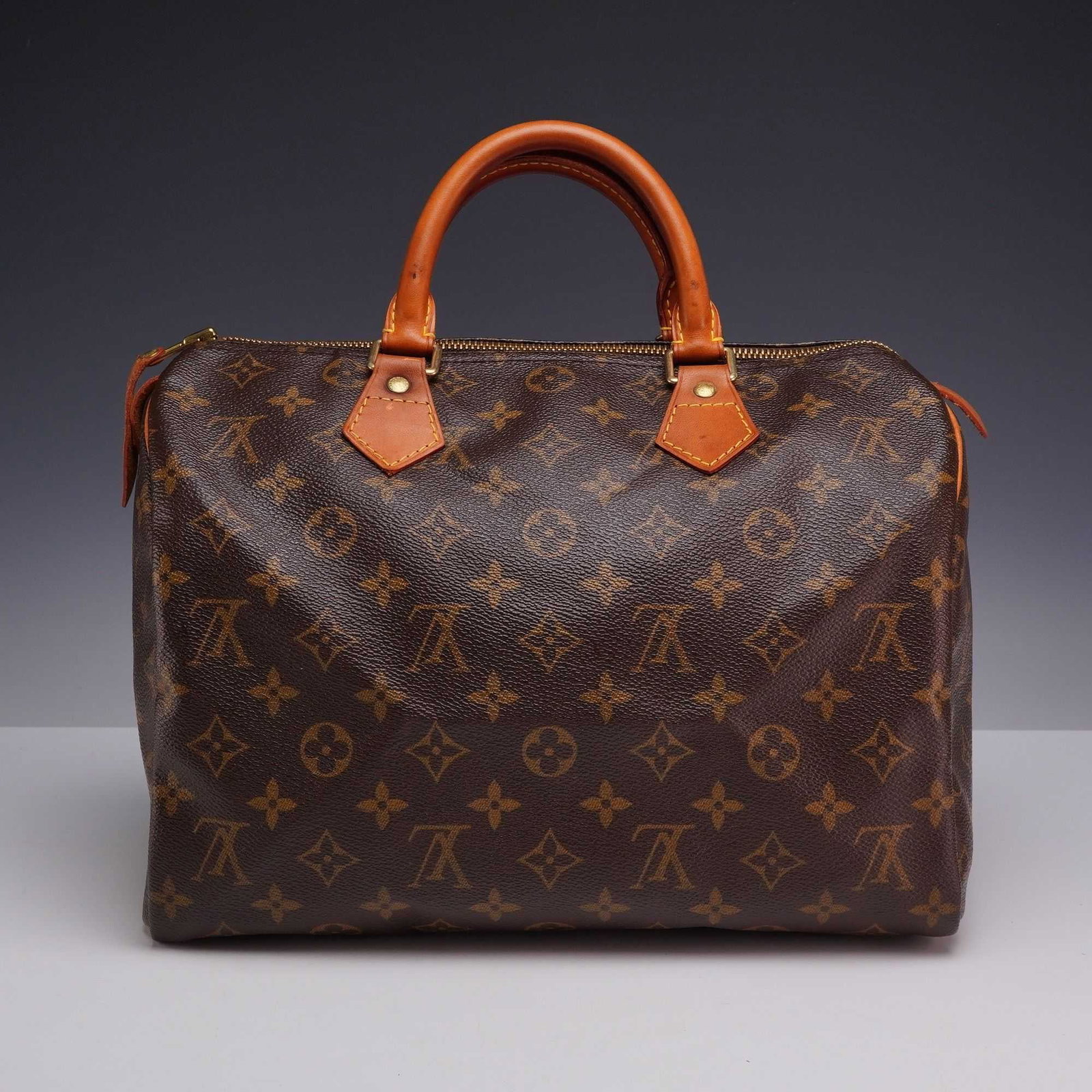 Louis Vuitton Monogram Speedy 30 Handbag: This classic handbag is finely crafted of traditional Louis Vuitton monogram coated canvas. The bag features vachetta cowhide rolled leather top handles and trim with polished gold-tone metal hardware