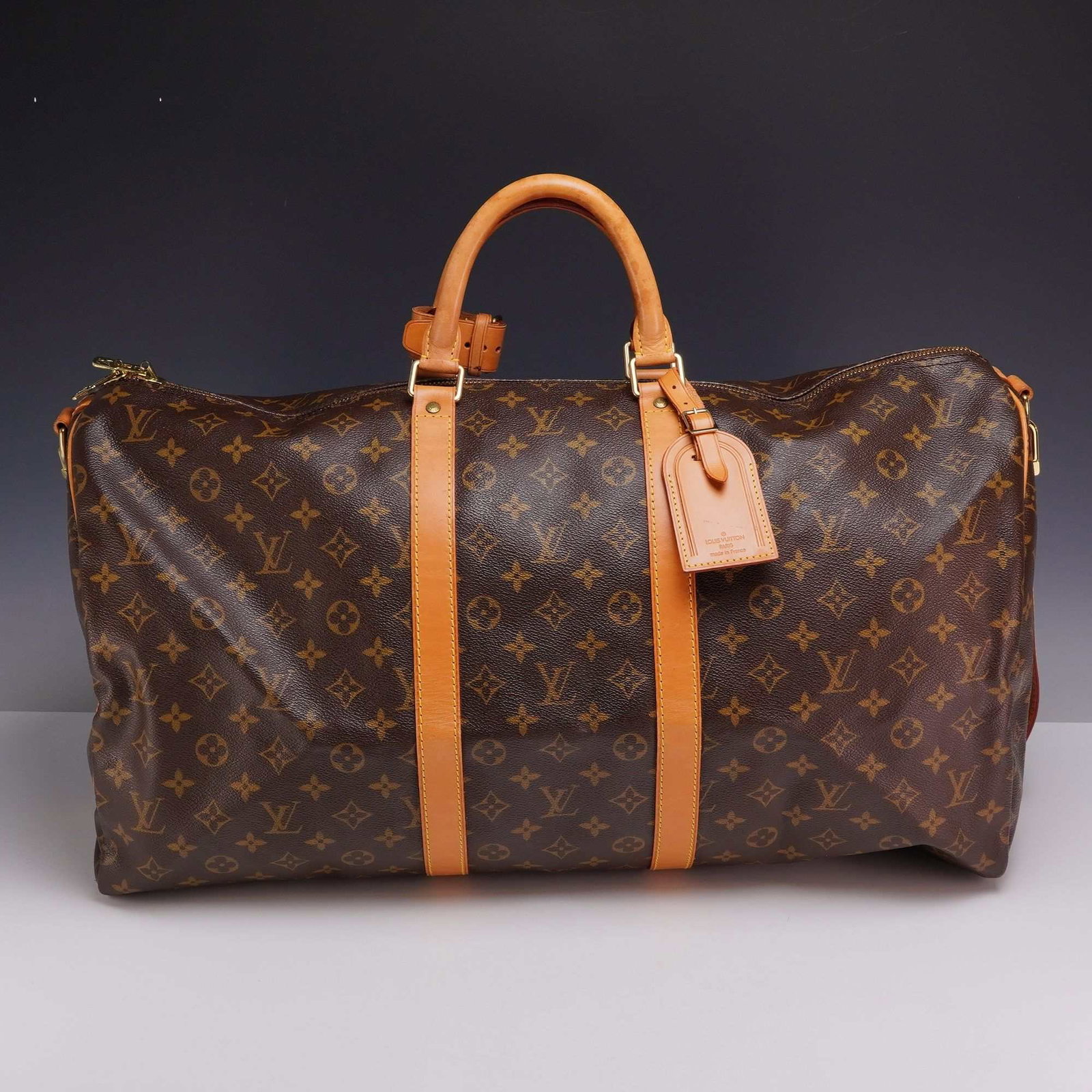 Louis Vuitton Monogram Keepall Bandouliere Travel Bag with Luggage Tag and Dust bag: A large Louis Vuitton Keepall Bandouliere travel bag featuring the house signature monogram coated canvas with natural cowhide leather Vachetta trim. The design includes rolled leather top handles, tw