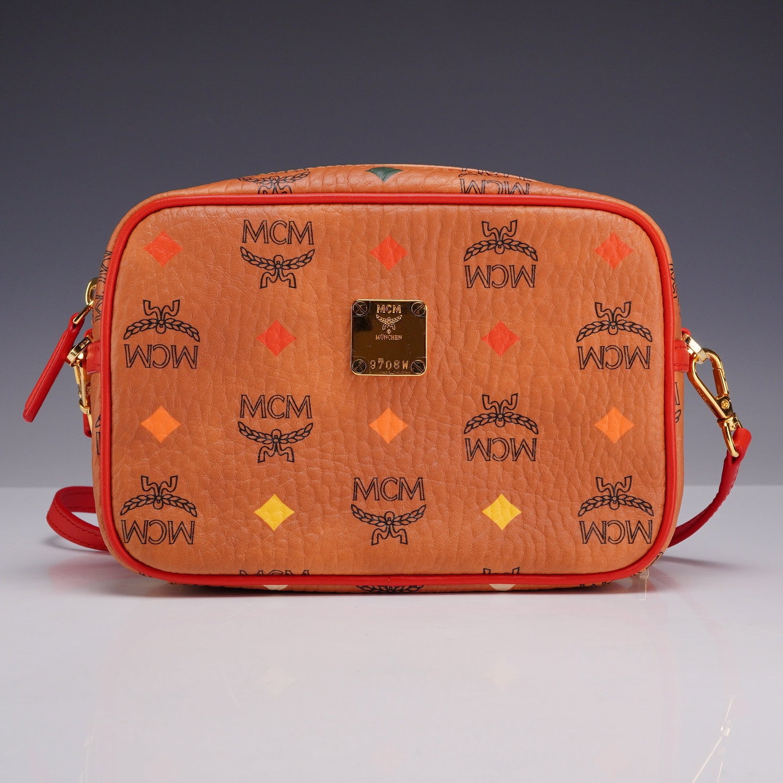MCM Skyoptic Visetos Spectrum Diamond Camera Crossbody Bag: An MCM Skyoptic Visetos Spectrum Diamond camera style crossbody bag crafted from the house's signature cognac coated canvas. The exterior features the classic black Visetos monogram print accented wit