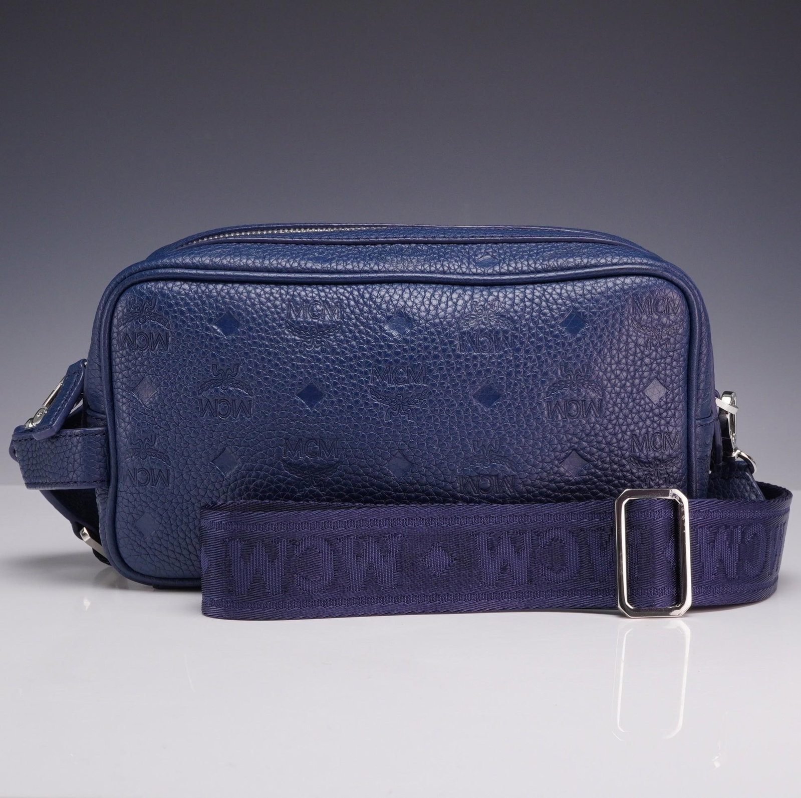 MCM Visetos Navy Blue Camera Crossbody Bag with Dust Bag: MCM Visetos navy blue camera crossbody bag. This structured rectangular camera bag is constructed from navy blue pebbled leather featuring an all-over embossed Visetos monogram pattern, consisting of 
