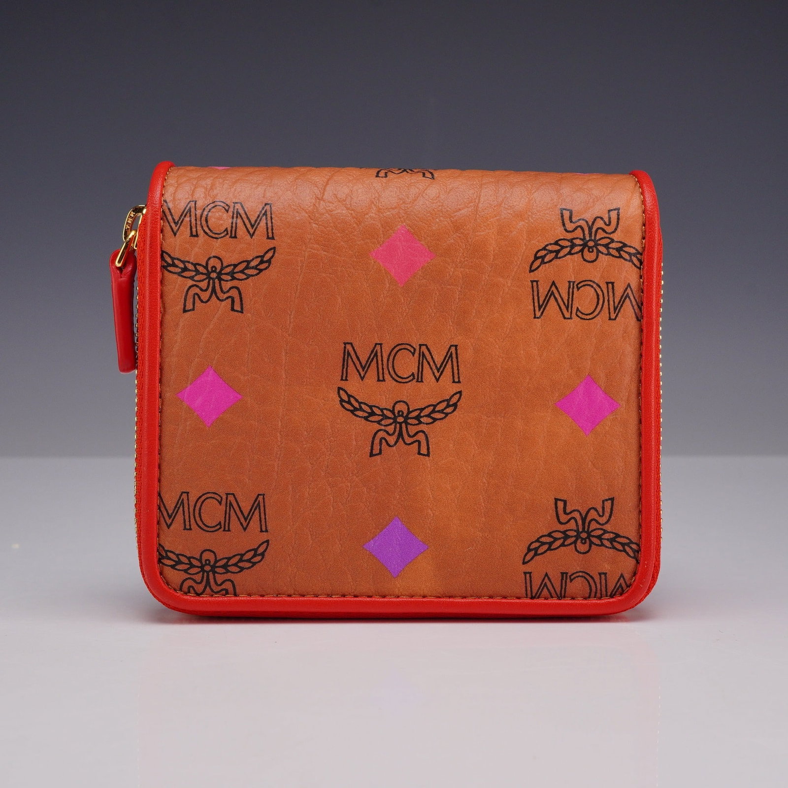 MCM Spectrum Diamond Visetos Mini Zip-Around Bifold Wallet in Cognac with Box and Dust Bag: This MCM bifold wallet is crafted from the signature cognac Visetos monogram coated canvas. The exterior is decorated with the Spectrum Diamond motif, featuring printed diamond accents in pink, yellow