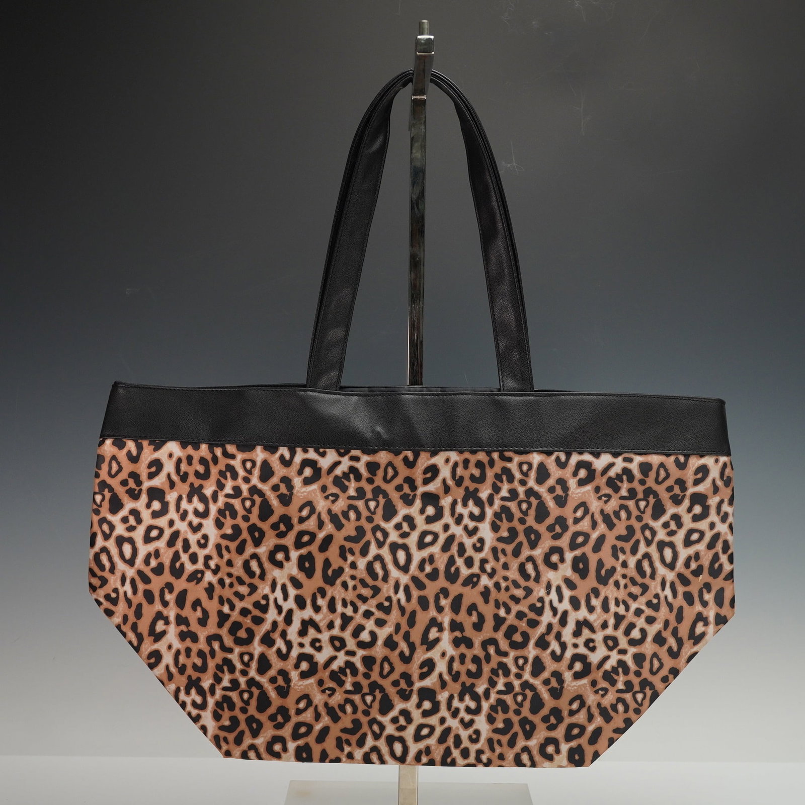 Bloomingdales Leopard Print Faux Leather Trim Tote Bag: A modern tote bag featuring a distinctive leopard print pattern across the main body, crafted from a waterproof material. It is designed with a black trim along the upper edge and two black top handle