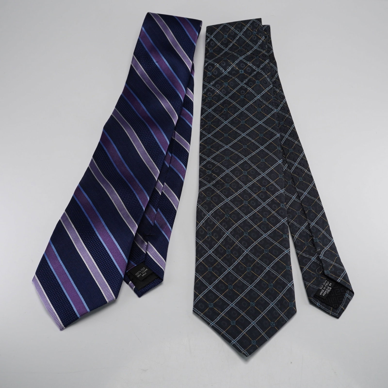 2pc Neiman Marcus and Givenchy Silk Neckties: This lot features two modern men neckties in 100% silk. The first tie, by Neiman Marcus, displays a diagonal stripe pattern in shades of navy blue, light blue, purple, and white. Its internal label co