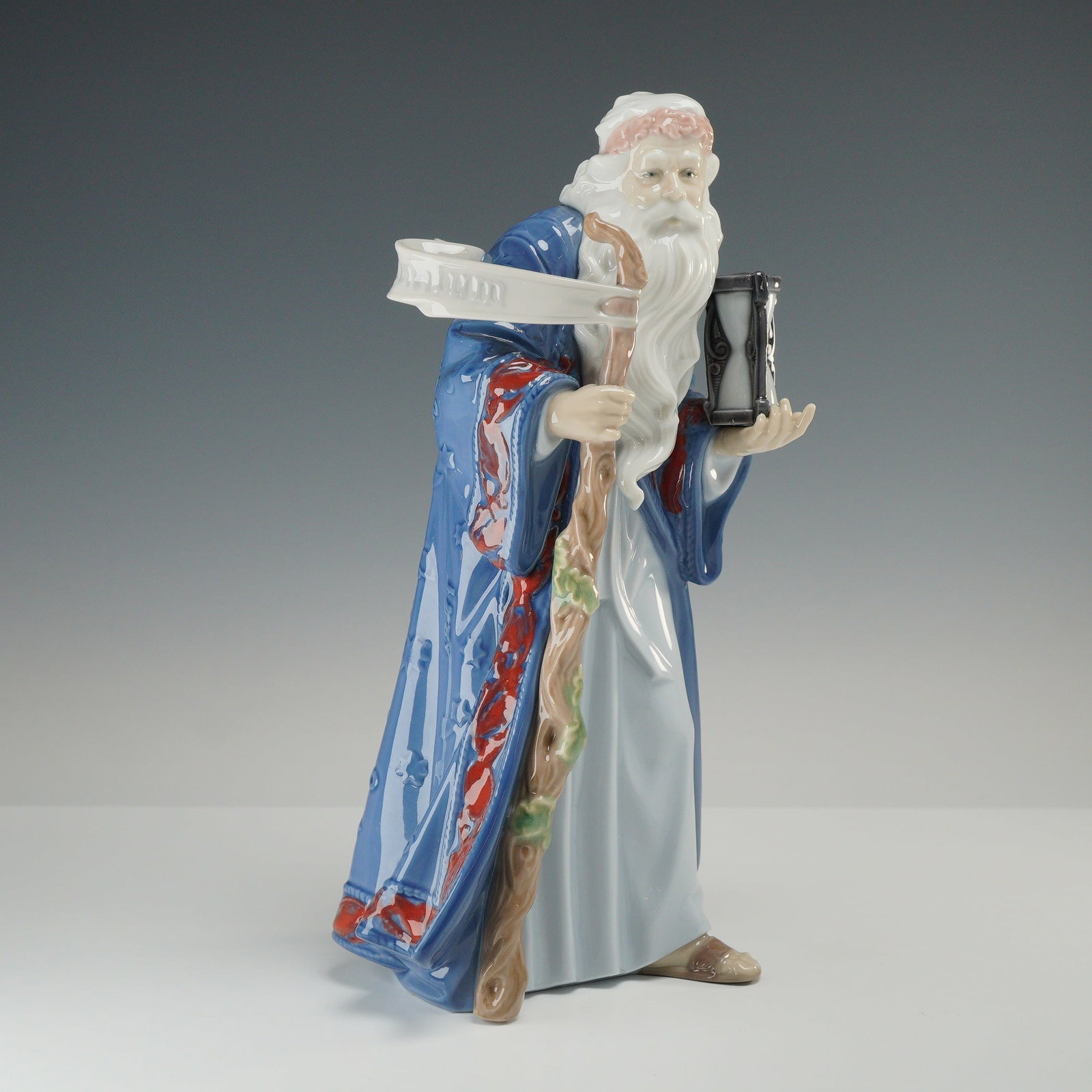 Lladro Inspiration Millennium Porcelain Figurine Father Time 01006696: This Lladro glazed porcelain figurine was designed by sculptor Juan Herrero as part of the Inspiration Millennium series issued in 1999. The sculpture depicts an elderly man with a long, flowing white