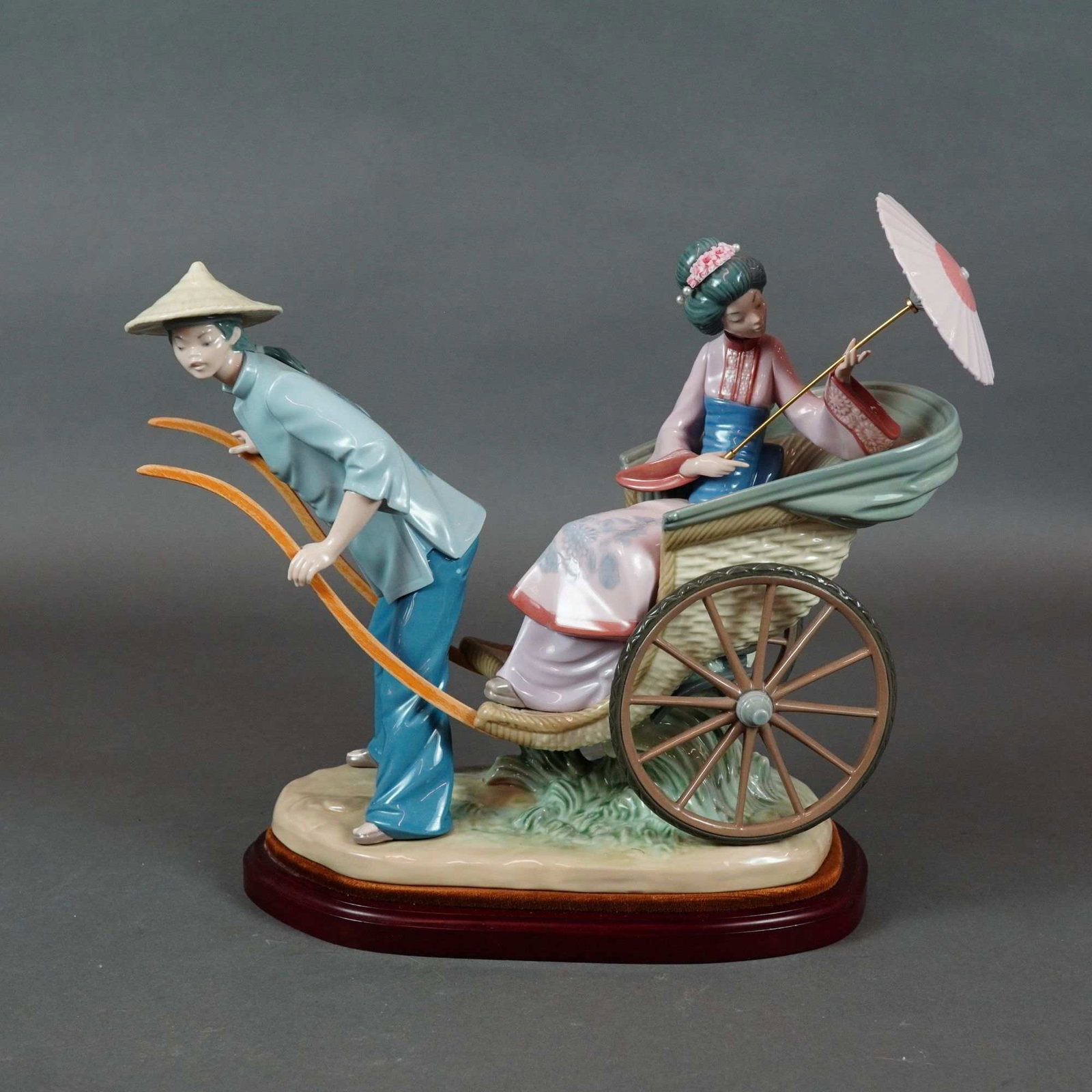 Lladro Porcelain Figurine with Base, A Rickshaw Ride 1001383 with Base: A large glazed porcelain figurine titled A Rickshaw Ride, model number 1383, produced by Lladro. This polychrome piece depicts a traditional Japanese scene featuring a male rickshaw puller and a femal
