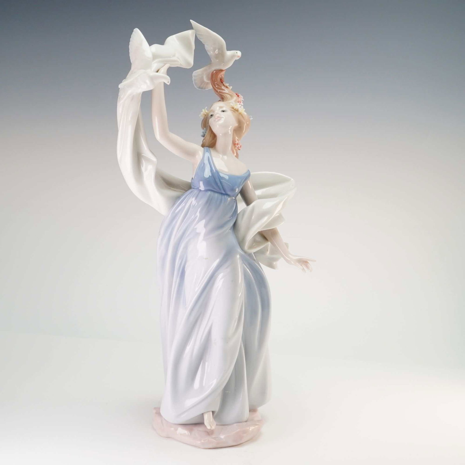 Lladro Porcelain Figurine, New Horizons 01006570: A Lladro glazed porcelain figurine titled New Horizons, part of the Inspiration Millennium collection. The figure depicts a young woman in a flowing, classically styled gown featuring a blue bodice an