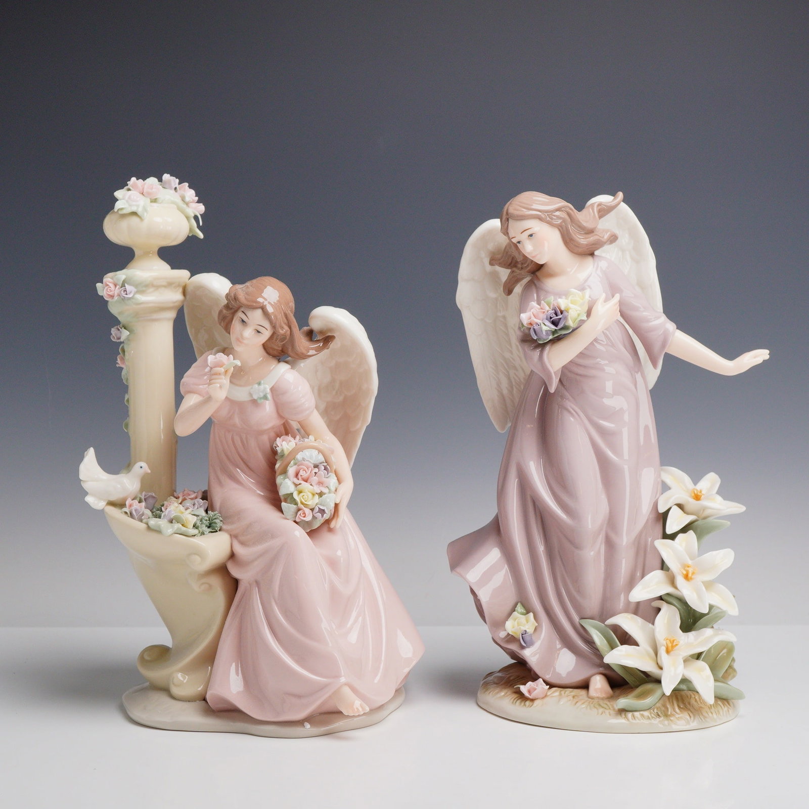 2pc Member's Mark Hand-Painted Porcelain Angel Figurines: This lot includes two hand-painted glazed porcelain angel figurines from Member's Mark. The first figure depicts a seated angel in a pink gown, resting on a cream-colored garden fountain or pedestal d